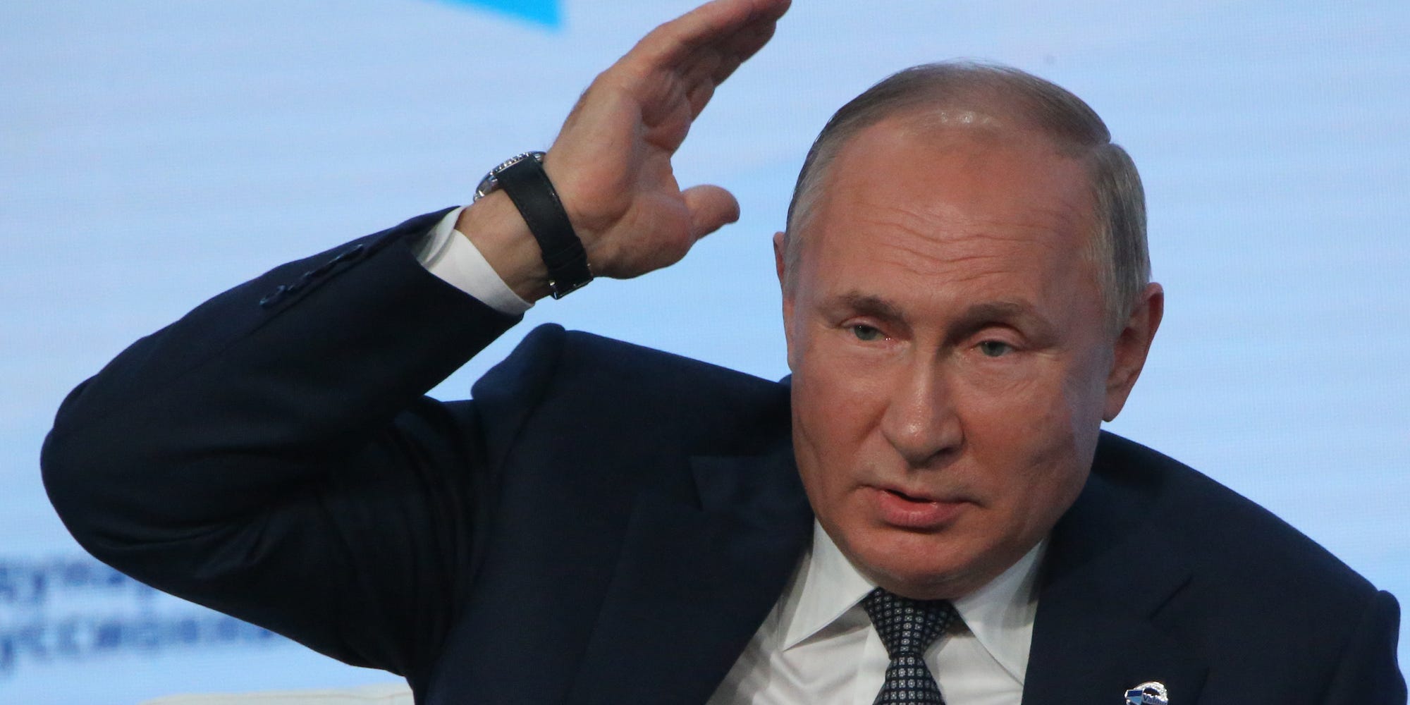Russian President Vladimir Putin raising his hand in a chopping motion.