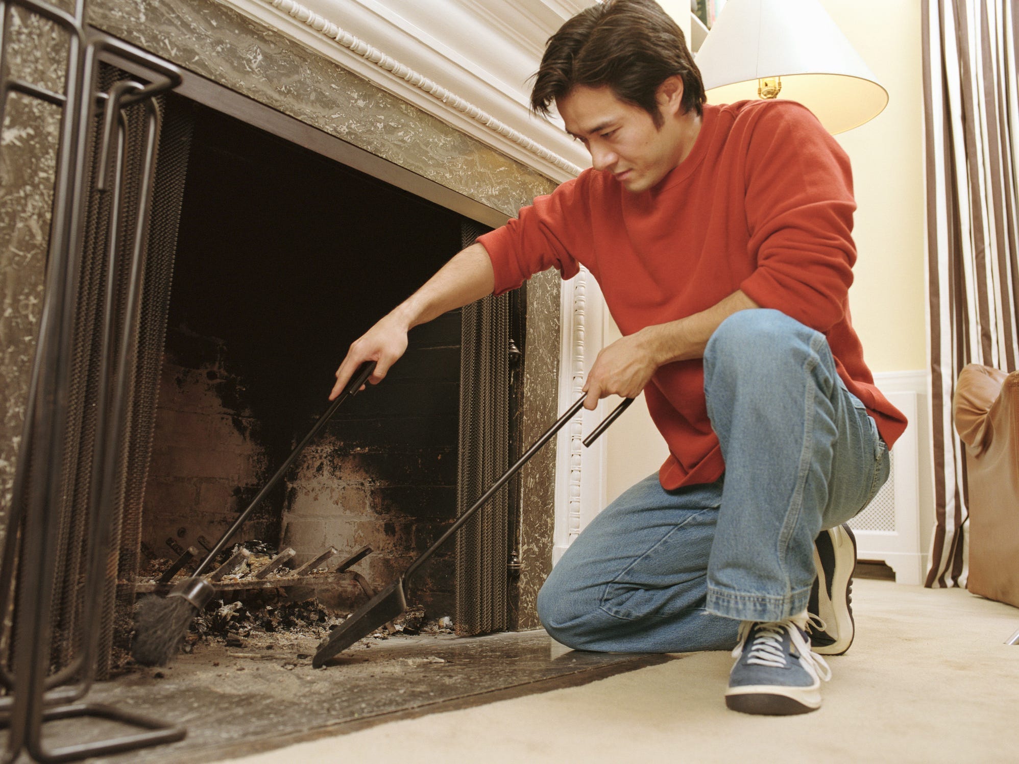 A man using a metal broom and shovel to sweep ashes out of a fireplace