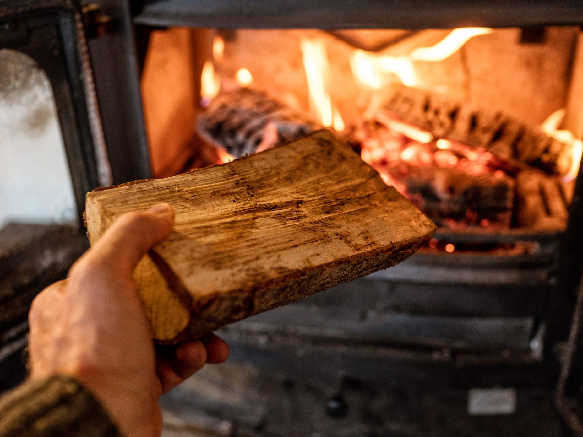 A hand placing a log onto a fire in a wood-burning stove