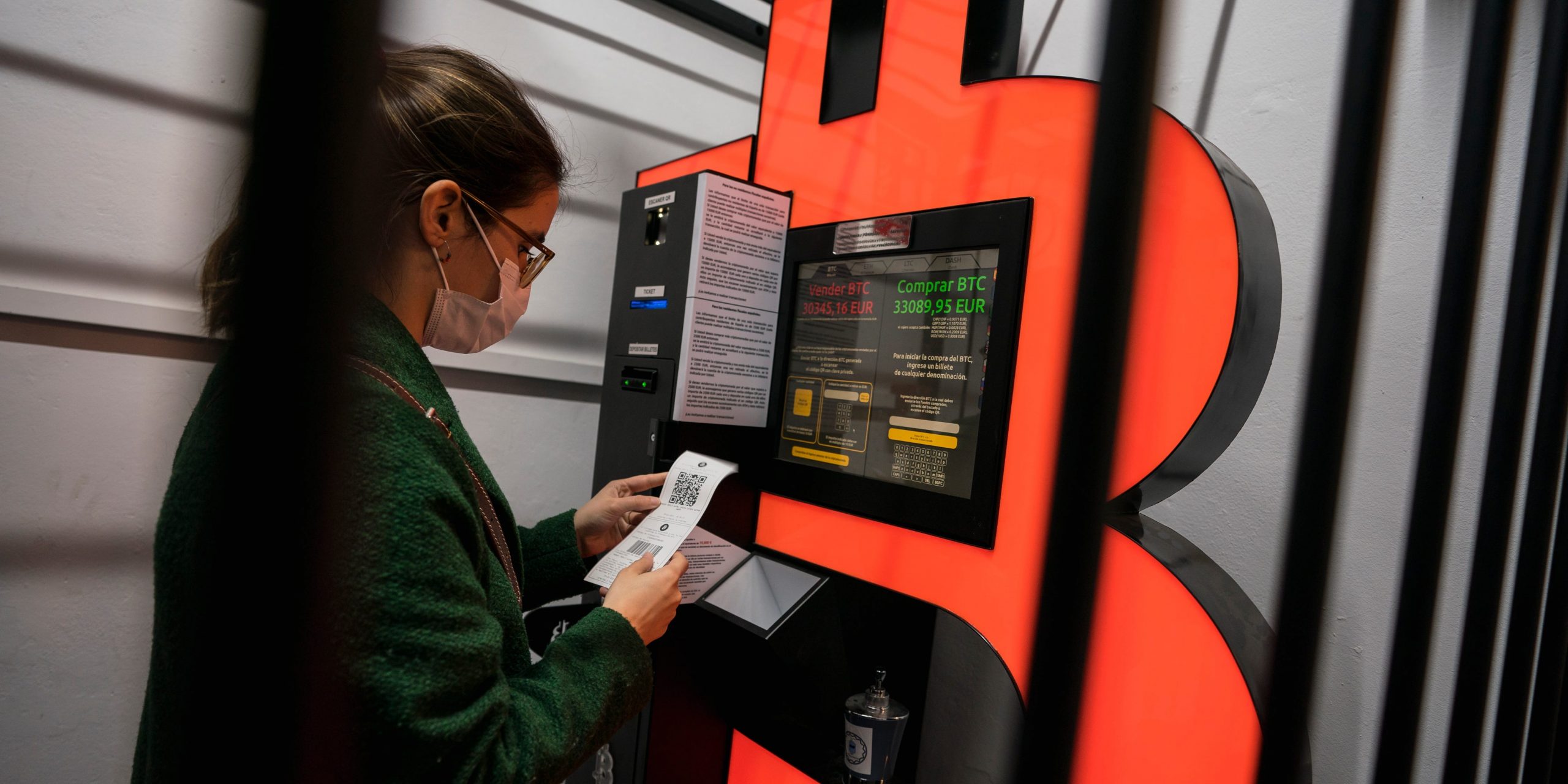 A woman uses a Bitcoin ATM machine placed within a safety cage on January 29, 2021 in Barcelona, Spain.