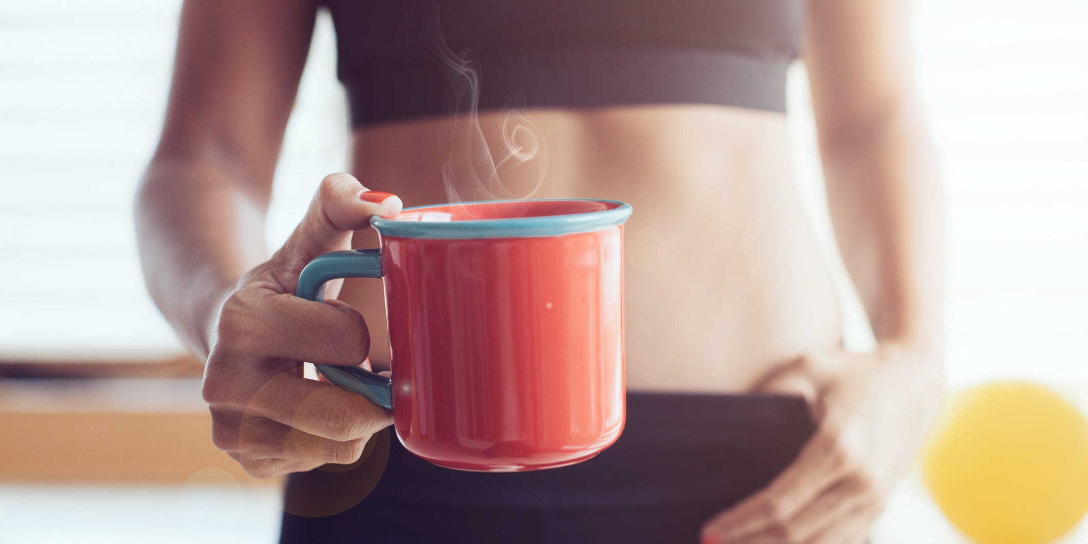A woman in workout attire holds a cup of coffee.