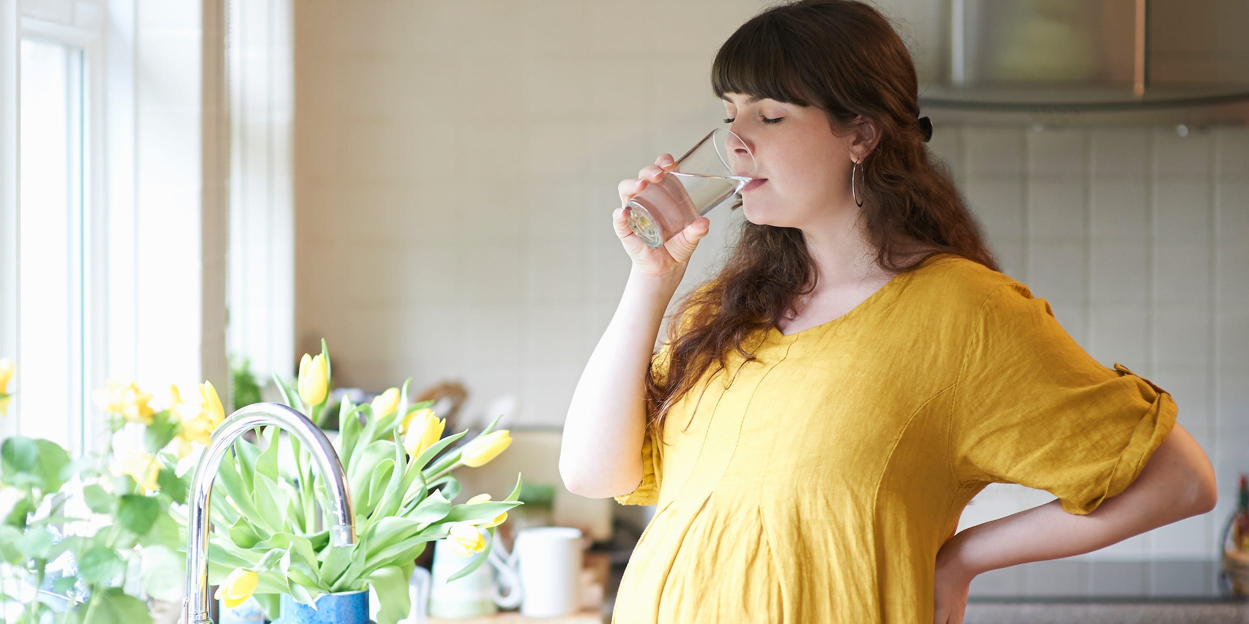 A pregnant woman drinks from a glass of water.