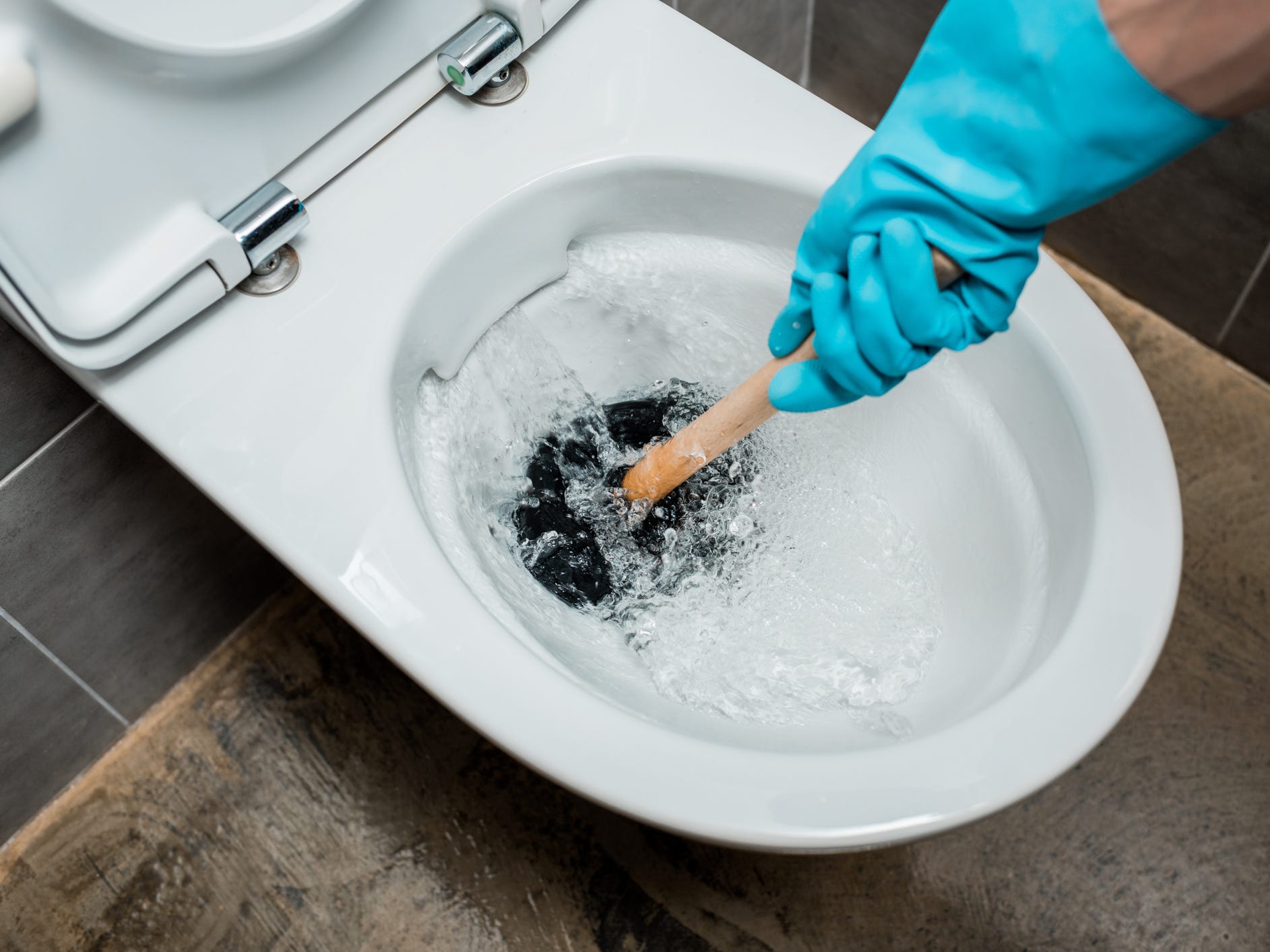 A hand in a blue cleaning glove using a plunger on a toilet