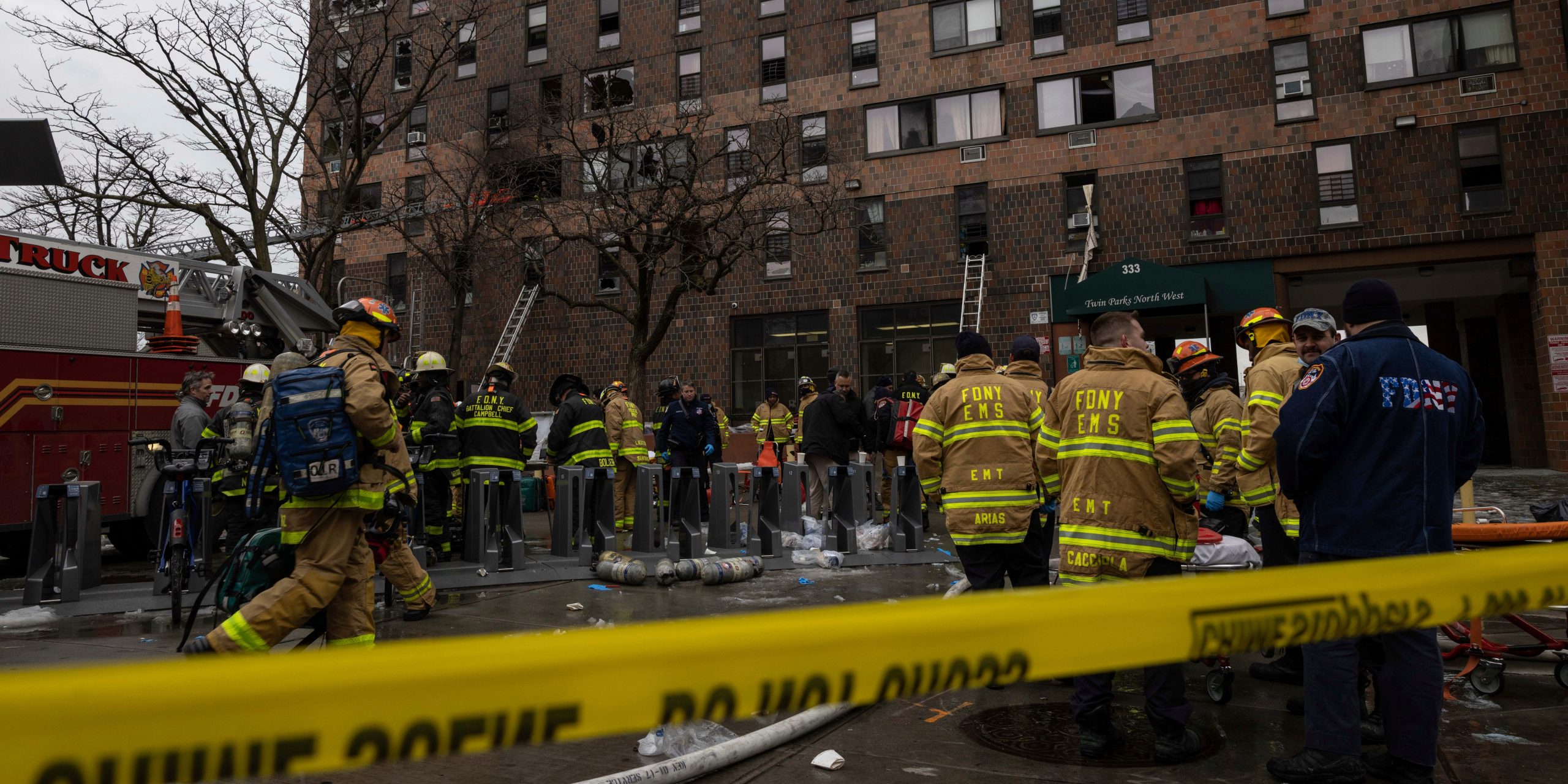 Firefighters stand in front of the Bronx apartment building where a Sunday fire killed 17 people.