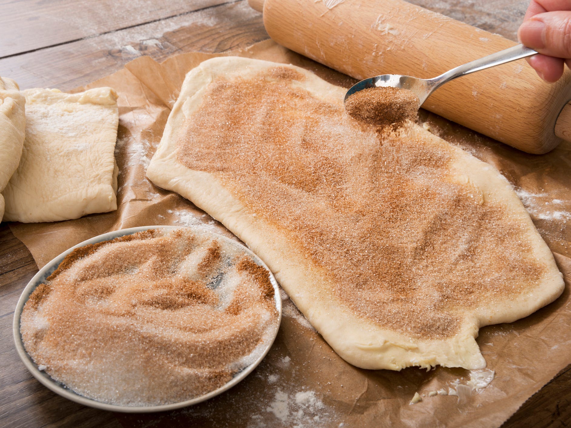 A hand using a spoon to sprinkle cinnamon sugar over rolled out pastry dough