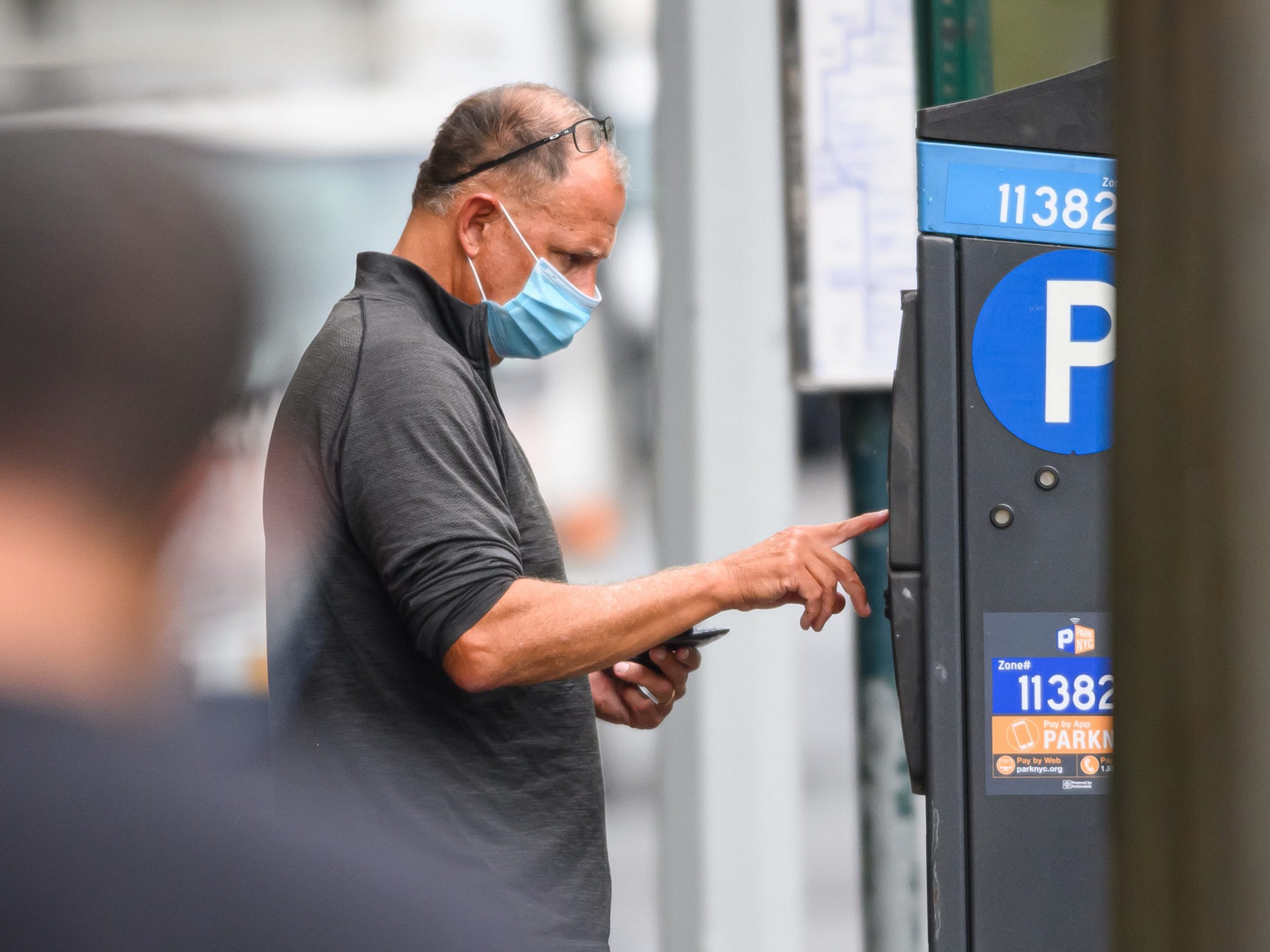 A man wearing a mask uses a parking meter.
