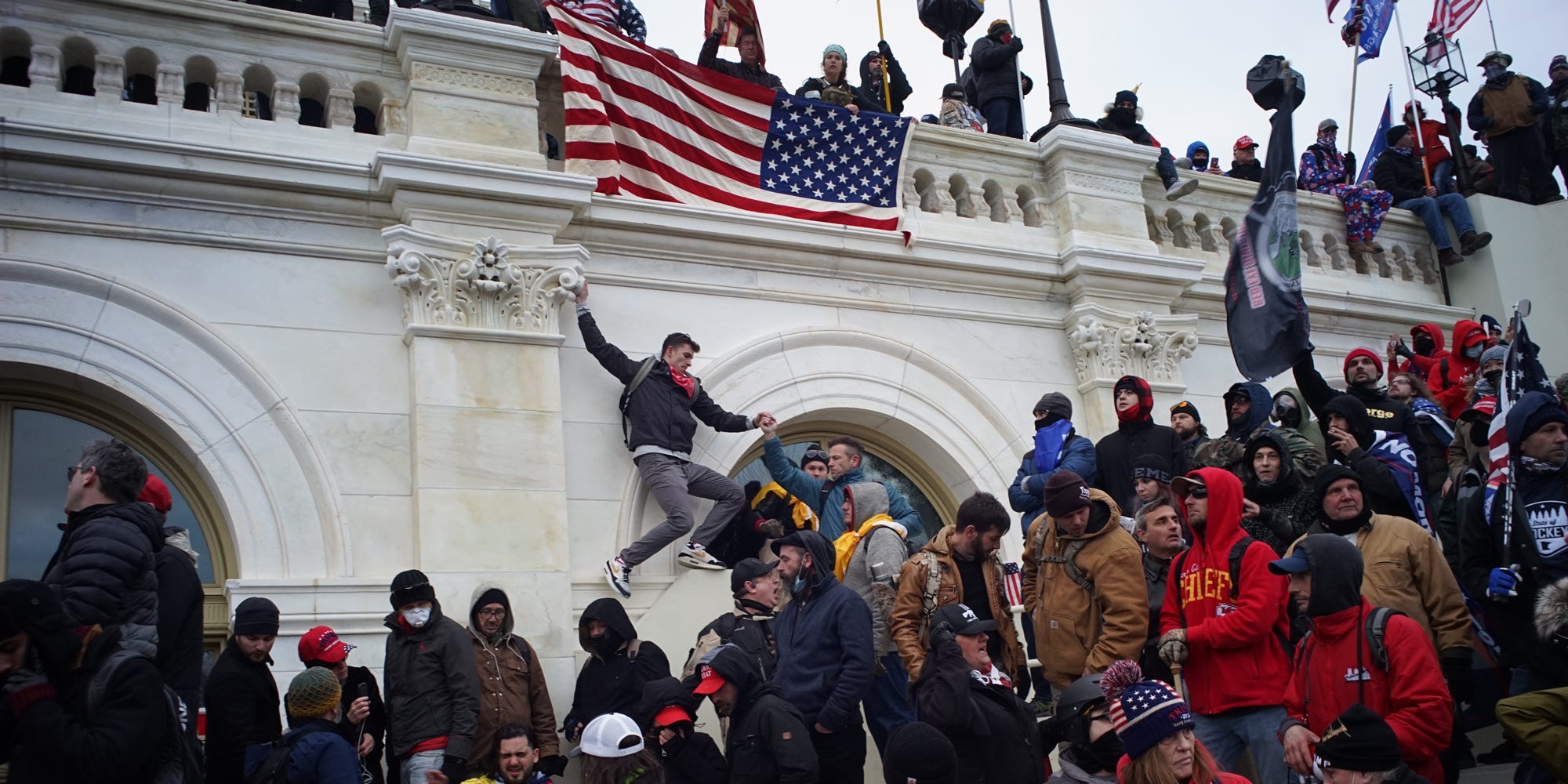 Someone is seen hanging from the Capitol facade beneath an American flag.