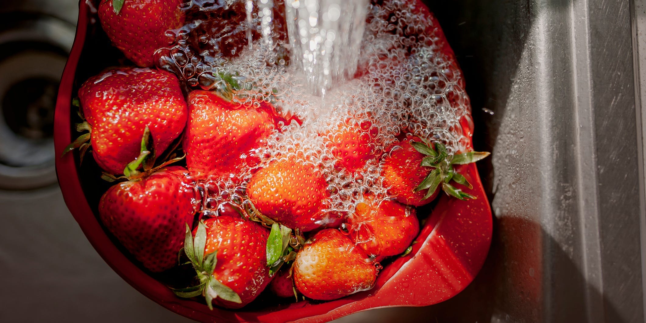 Strawberries being soaked in the sink with water running on top.