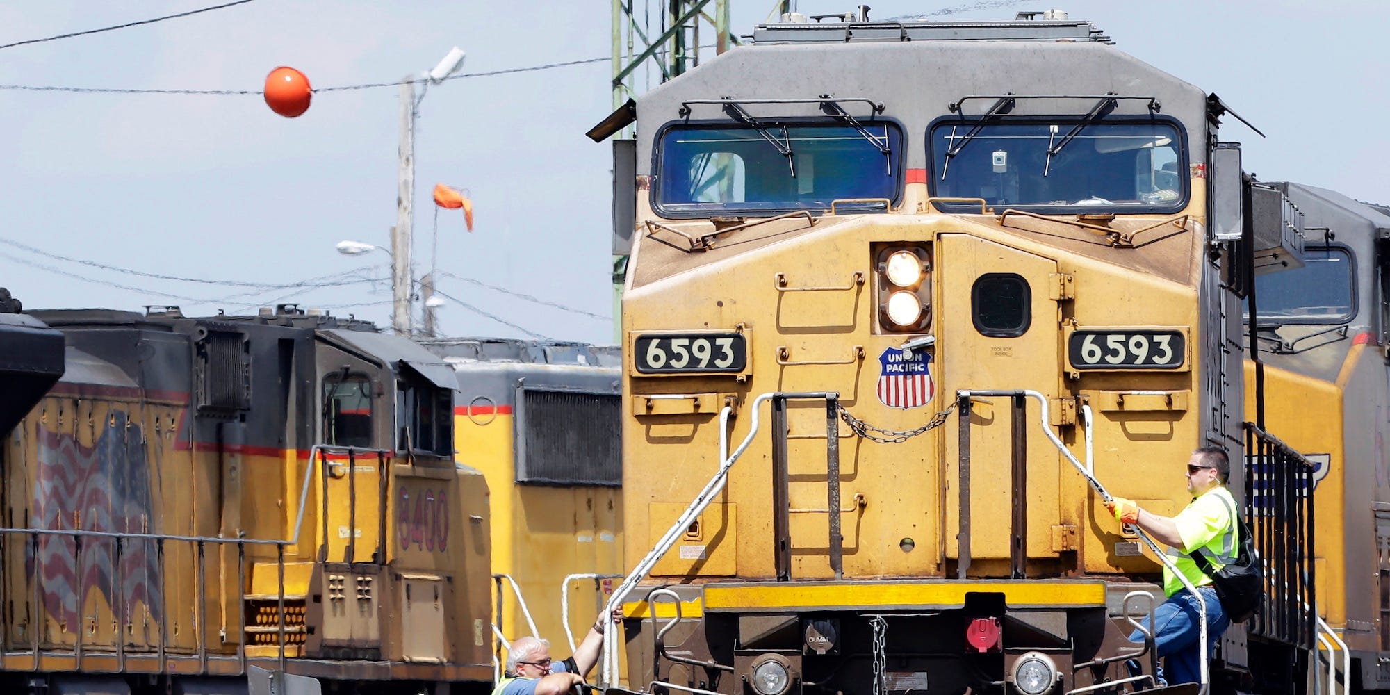 A yellow United Pacific train viewed from the front. Two men in hi-vis jackets cling to the sides.