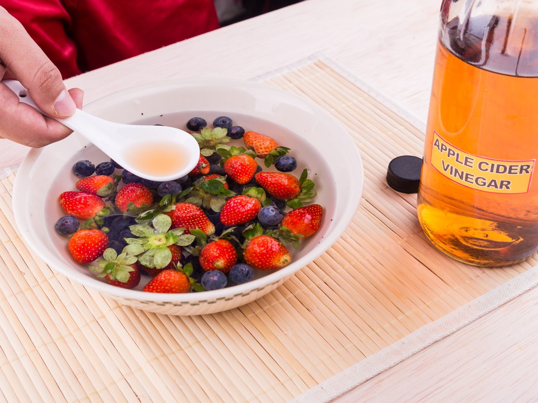 Berries in a bowl with water and a bottle of apple cider vinegar on the side