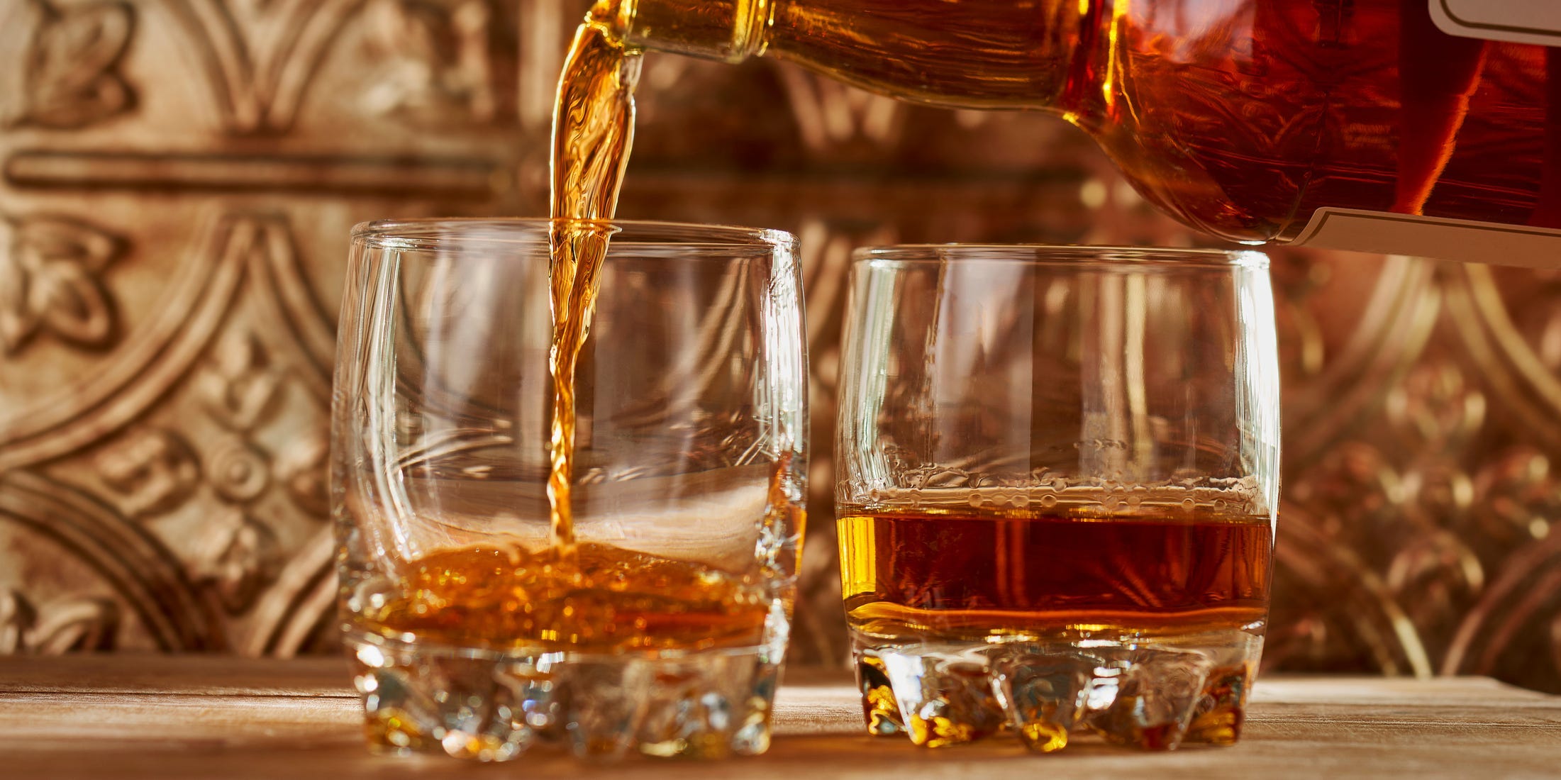 Whiskey being poured into two rocks glasses on a bar