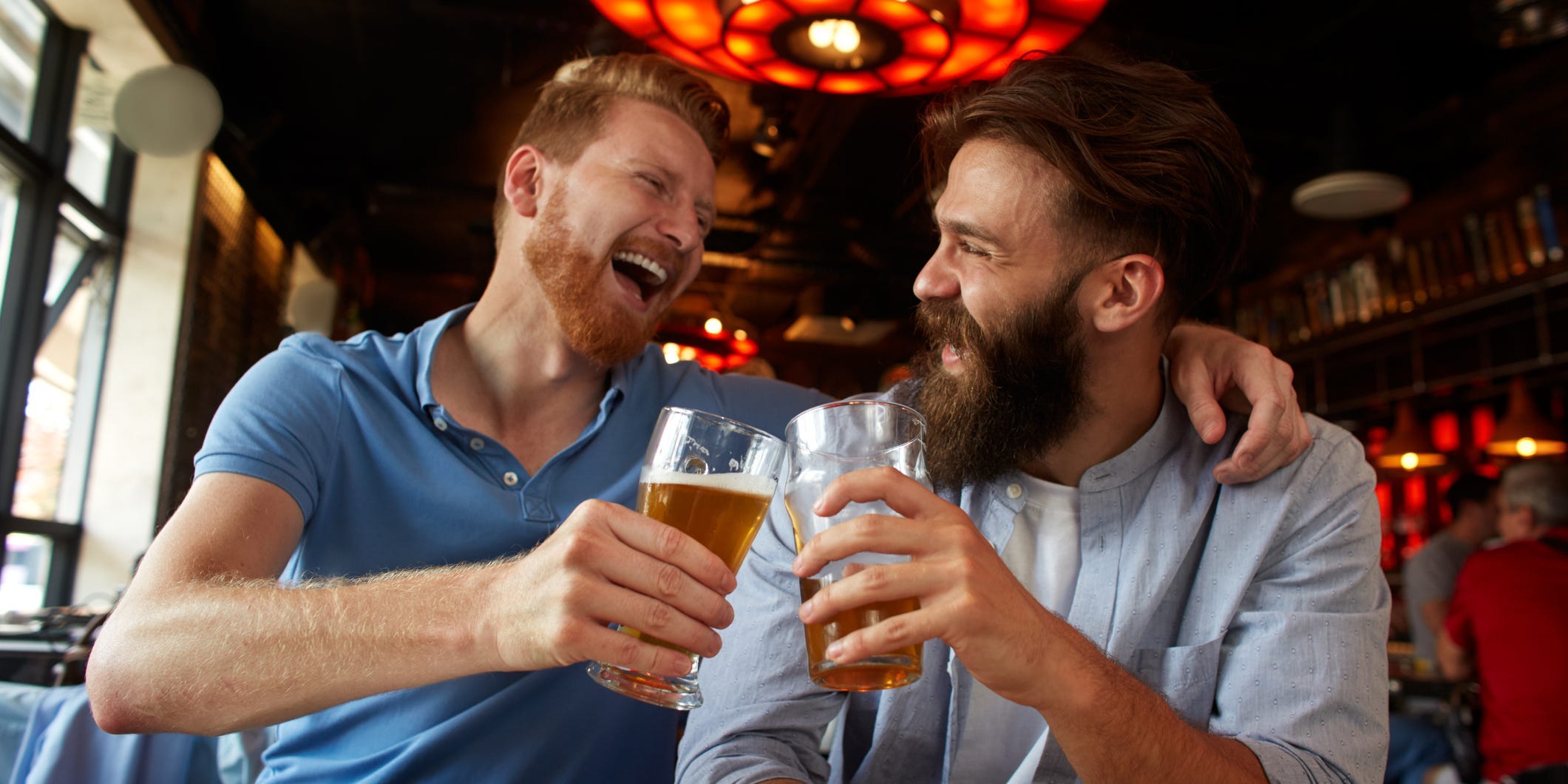 Two men sit close together at a brewery drinking beer and laughing together.