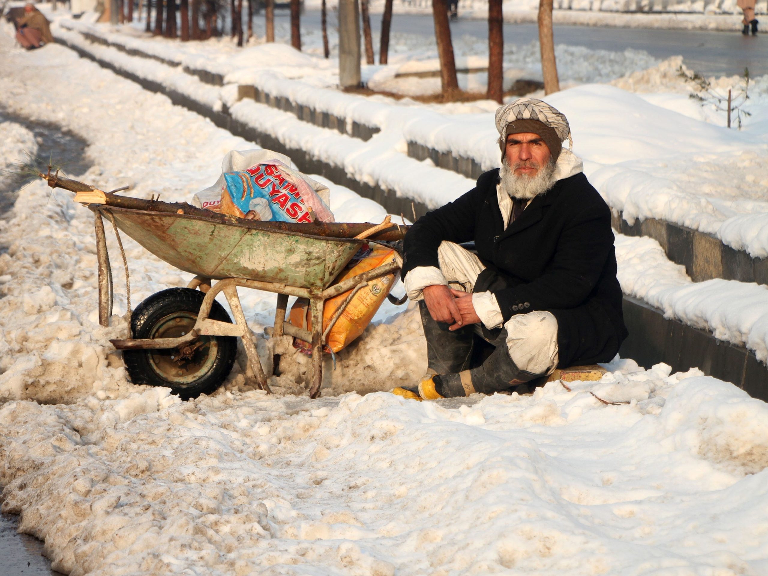 Afghan man sits in the snow as he waits for work.