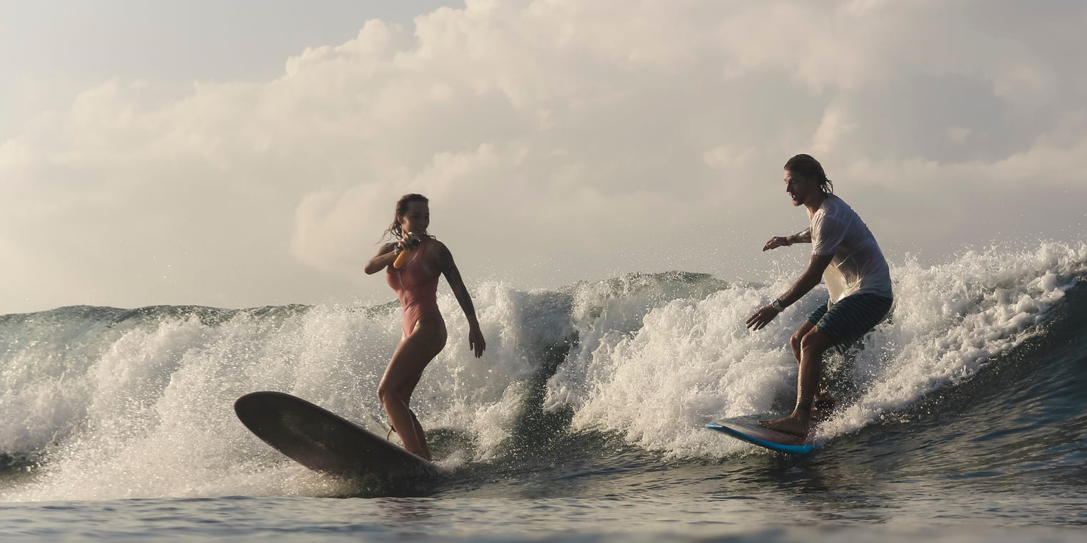A couple surfs a wave.