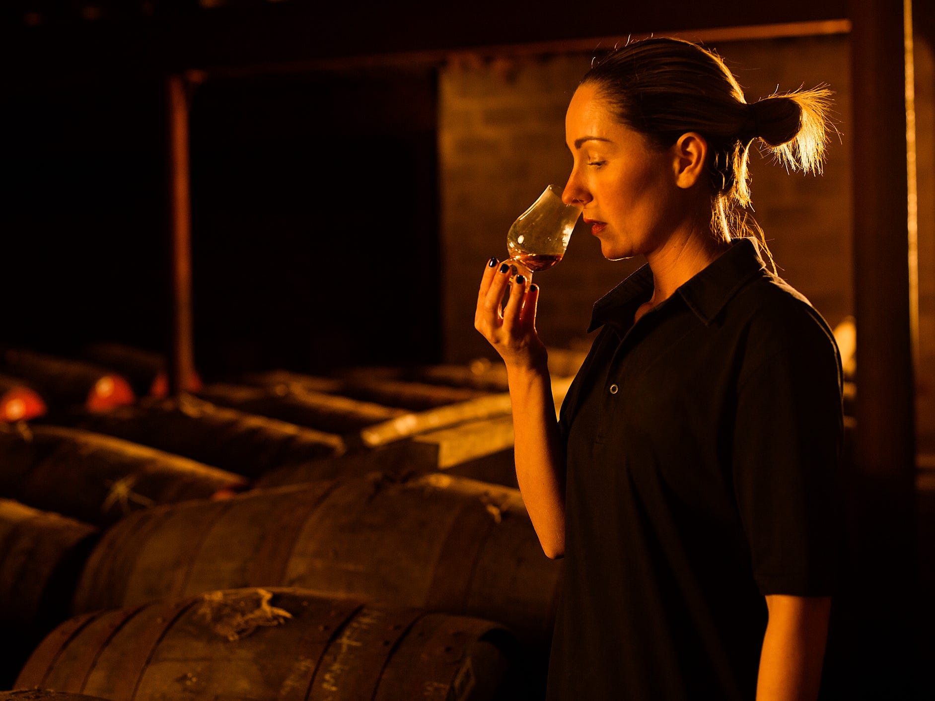 A woman smelling a snifter of Scotch whisky at a distillery