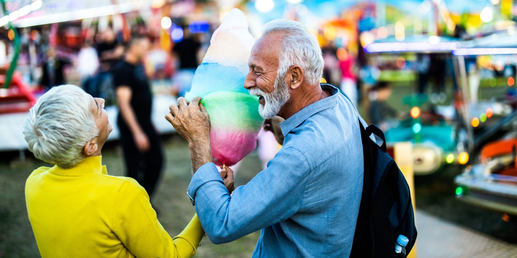 A couple at a carnival shares cotton candy.