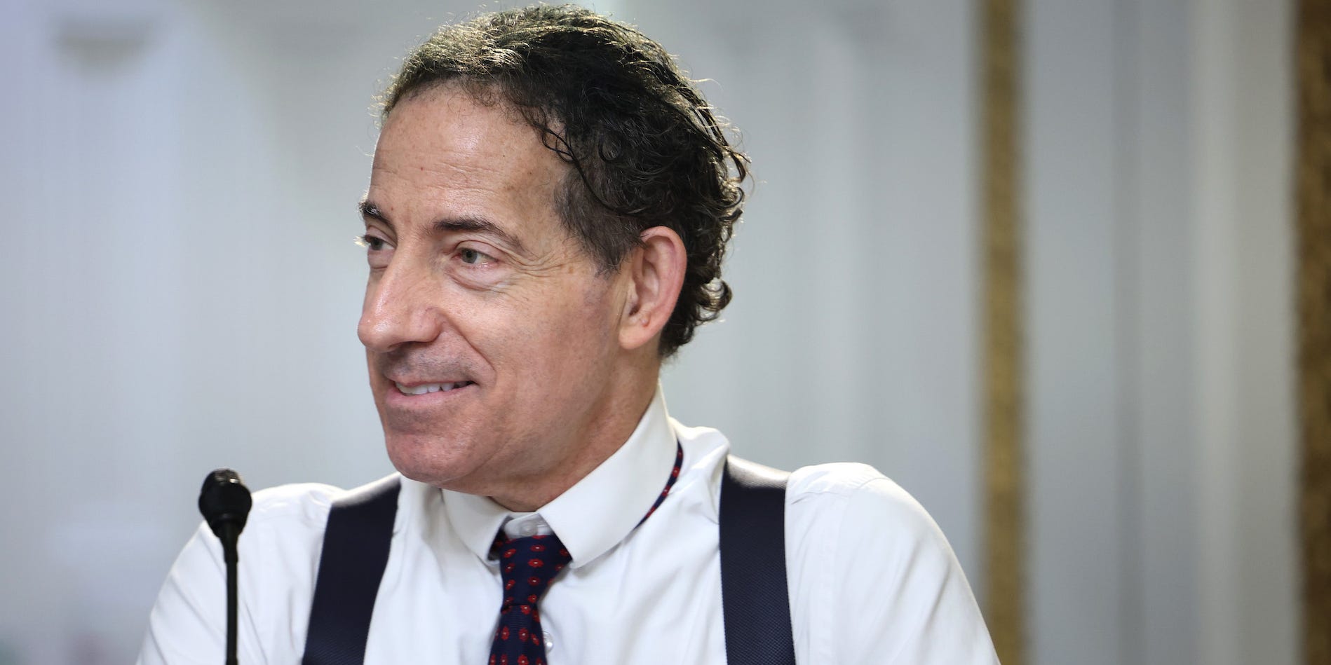 Congressman Jamie Raskin sits behind a podium wearing a white shirt, black suspenders and a black tie.