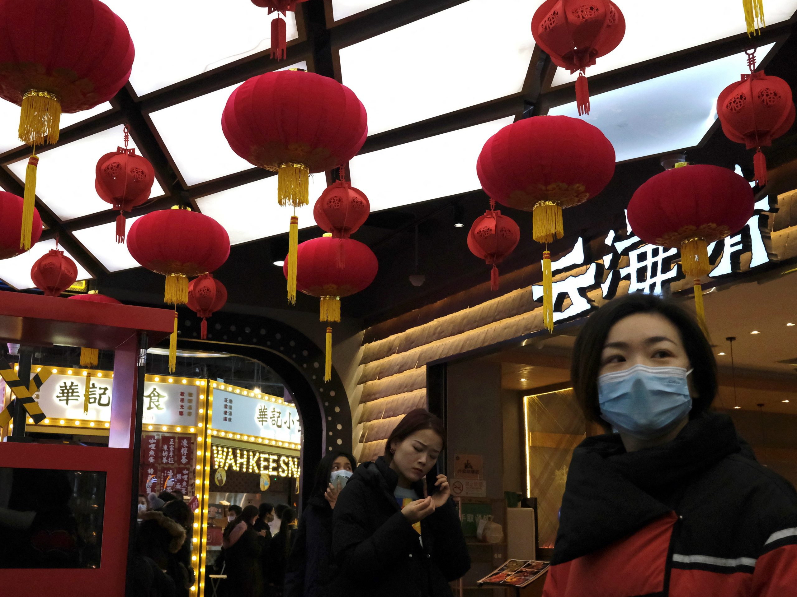Two women in face masks walking under lanterns decorating a food court inside a shopping mall, in Beijing, China