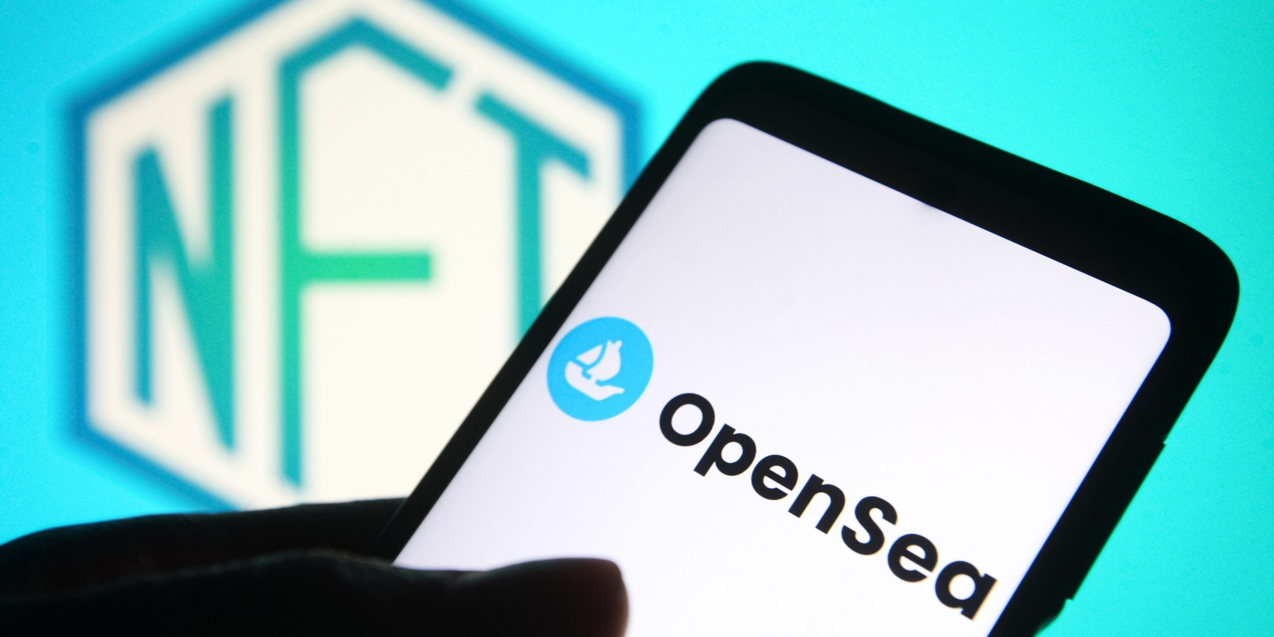 An OpenSea logo of an online marketplace for non-fungible tokens is seen on a smartphone screen and a NFT (Non-fungible token) sign in the background.