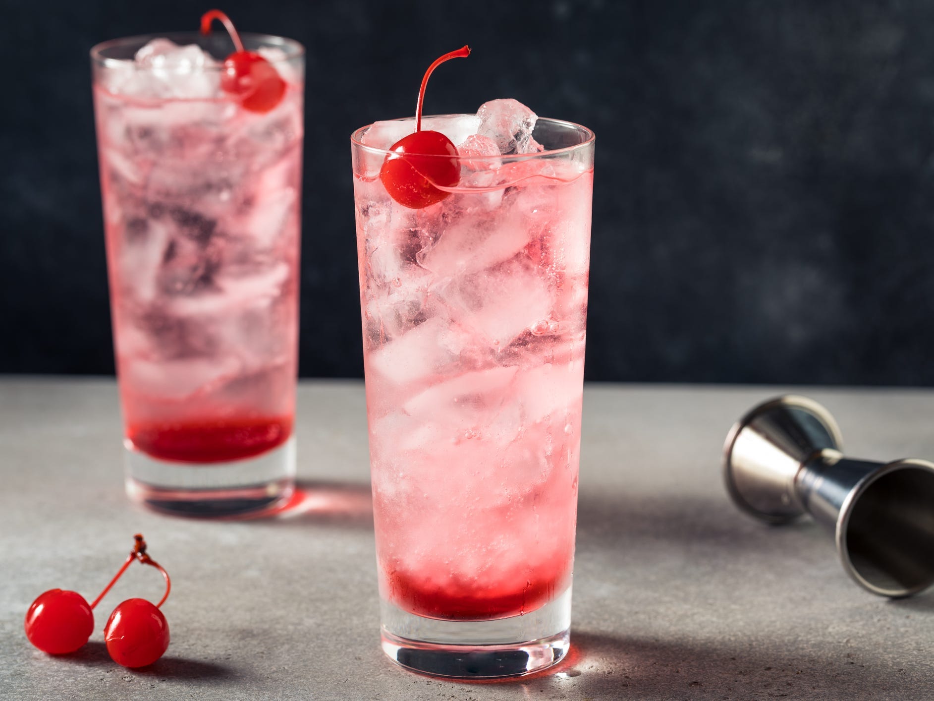 Two pink Shirley Temples in highball glasses garnished with cherries