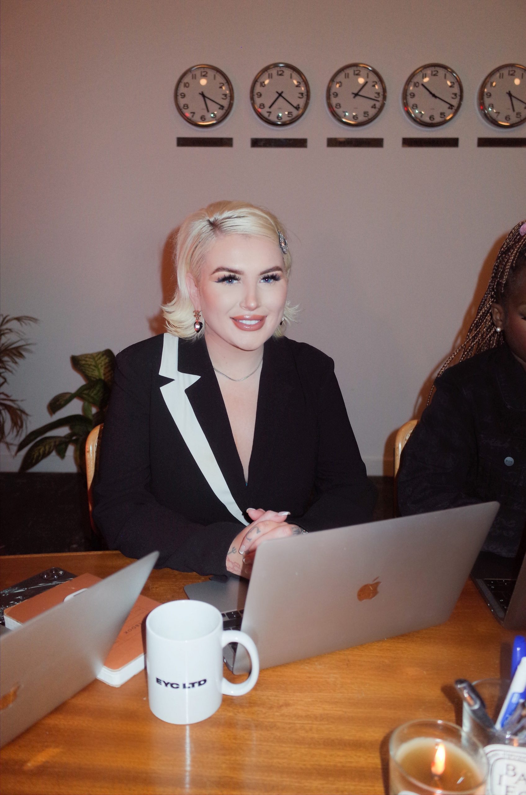 A woman in a black blazer sits smiling to the camera