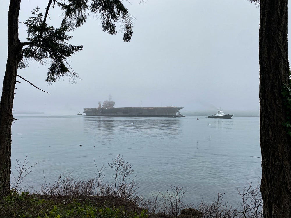 Navy tug boats support the USS Kitty Hawk’s towing in its final transit from a Naval Base in Kitsap, Washington to a ship-breaking facility in Brownsville, Texas.