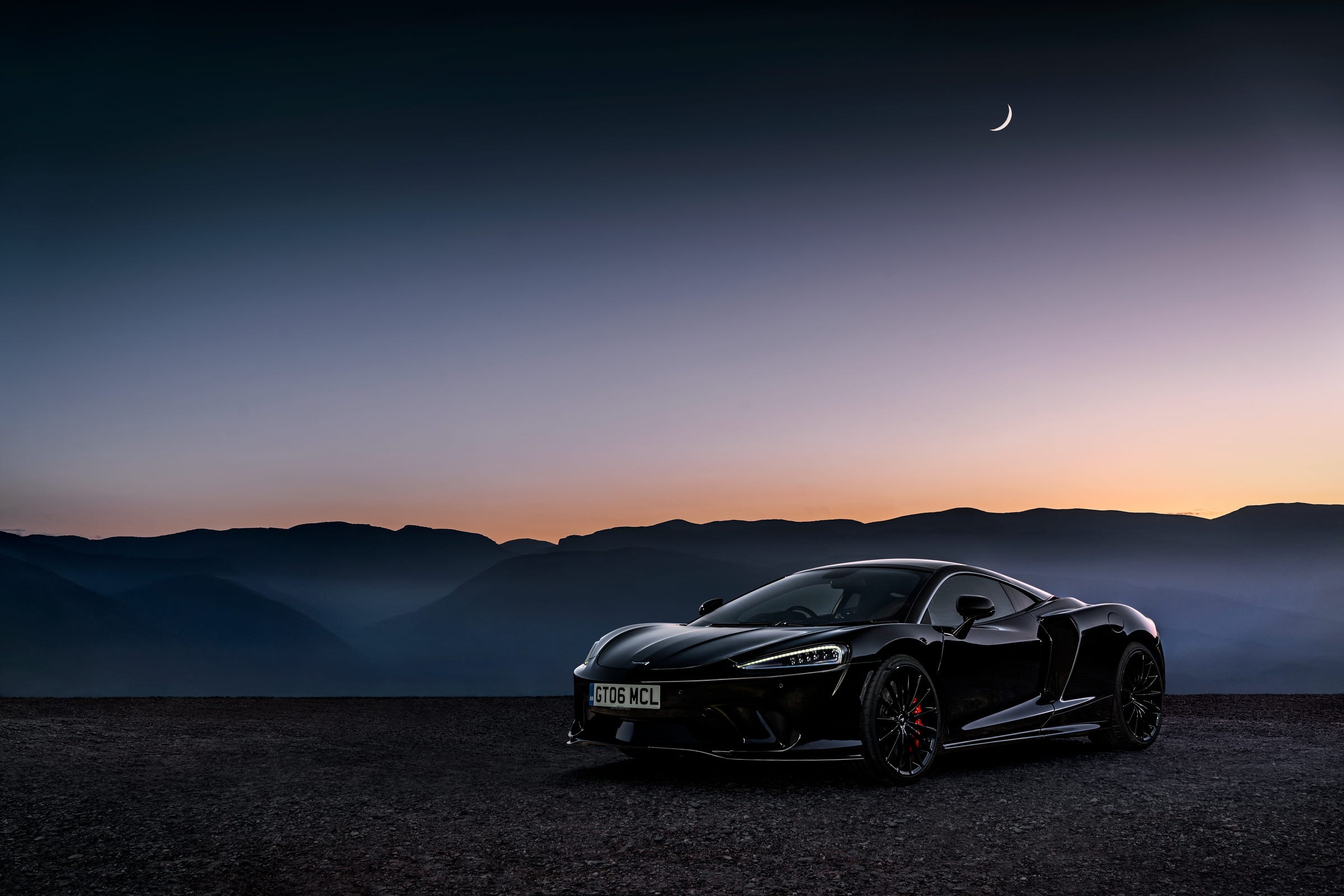 A black McLaren GT in front of a sunset and mountain range.