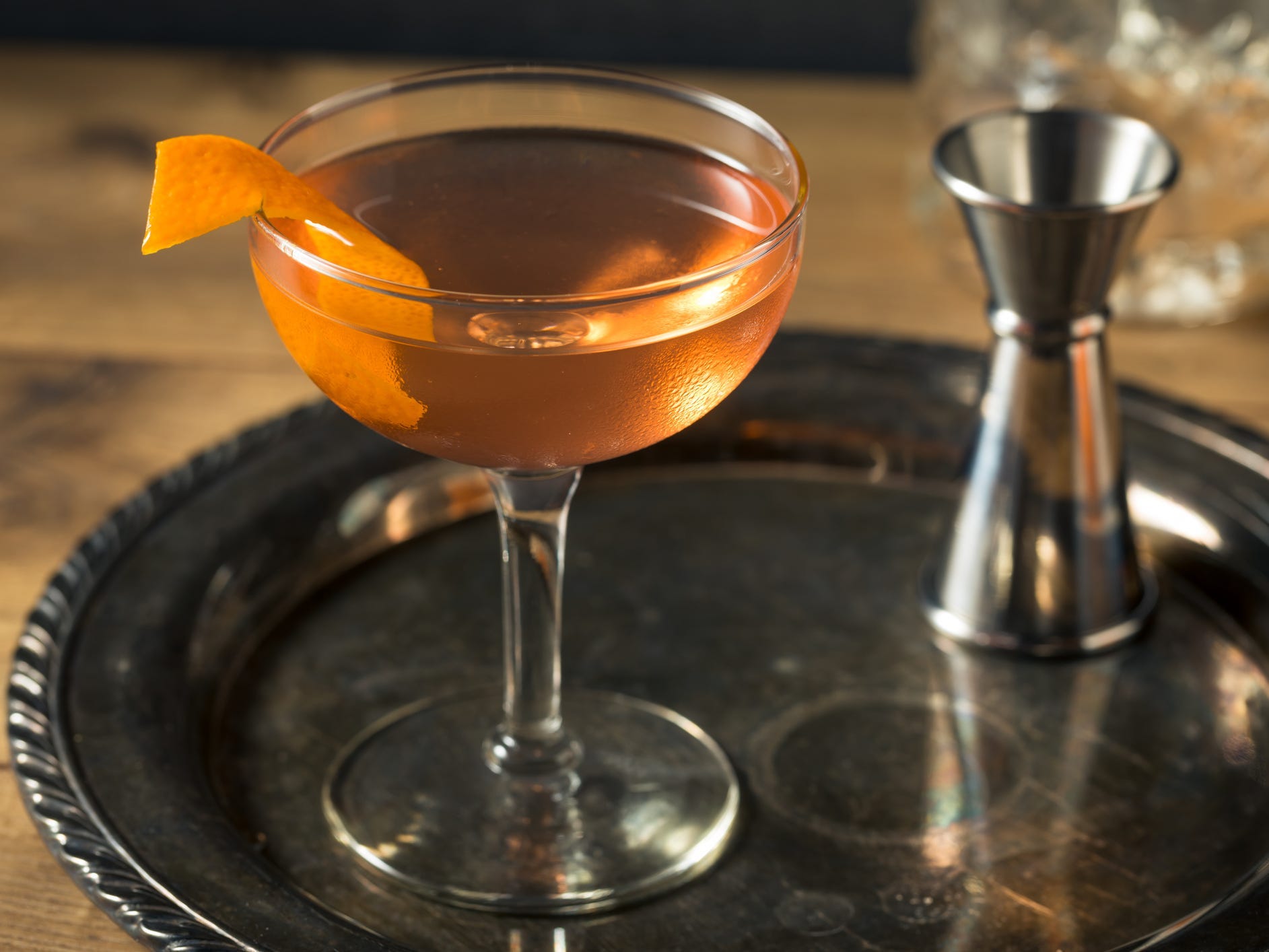 An orange-hued el presidente cocktails garnished with orange peel sitting on a silver tray