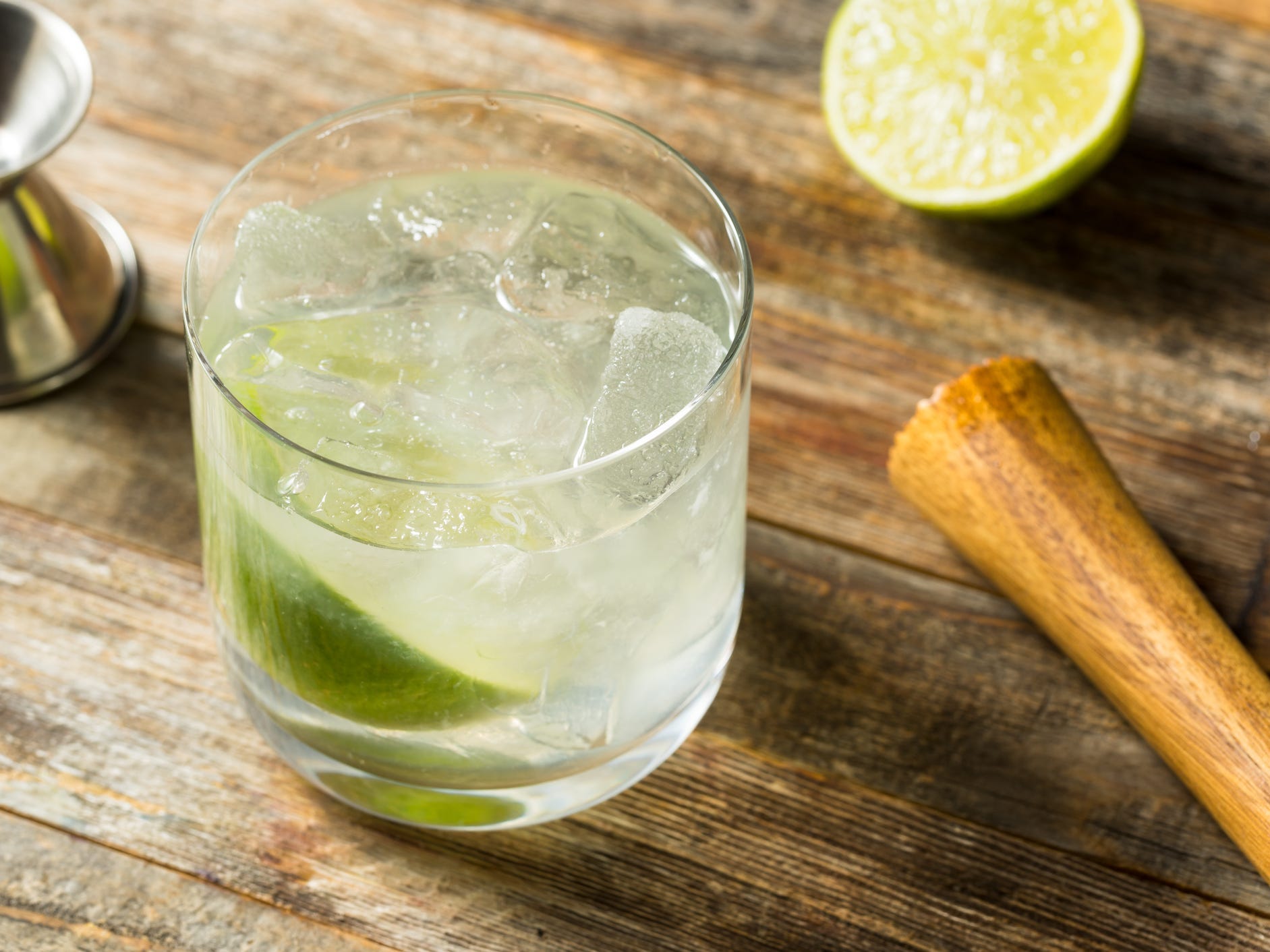 A ti' punch cocktail sitting next to a muddler, a jigger, and a lime half