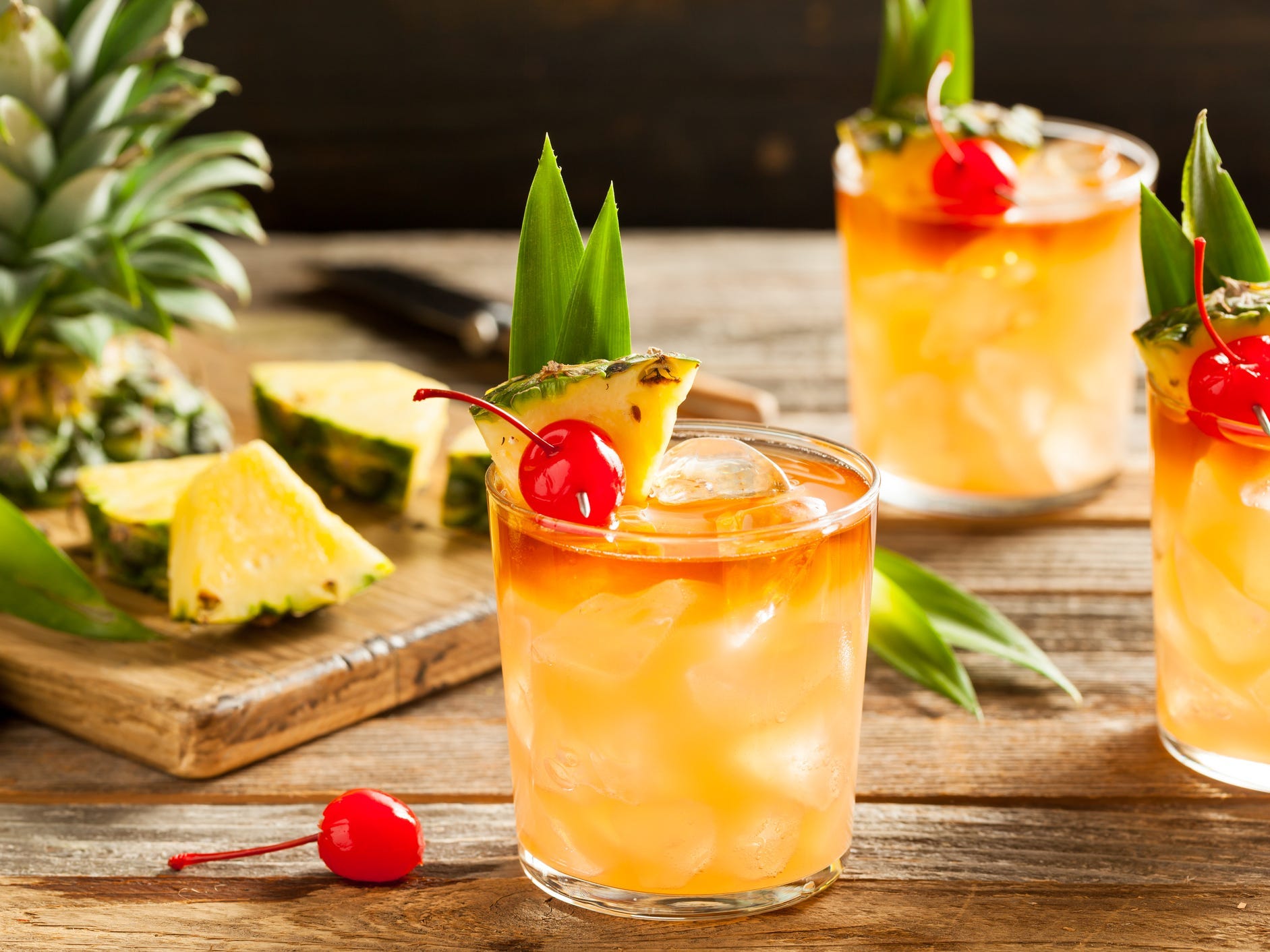 Three mai tai cocktails garnished with pineapple and cherry