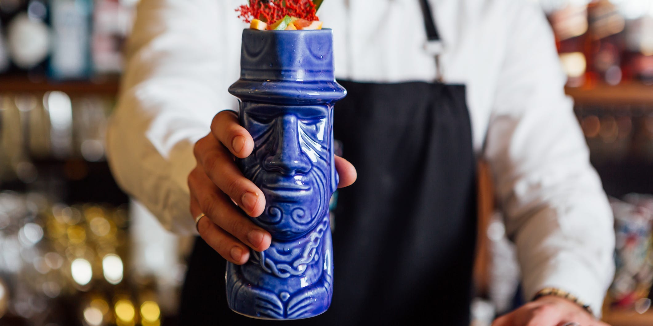 A bartender serving a drink in a blue tiki mug