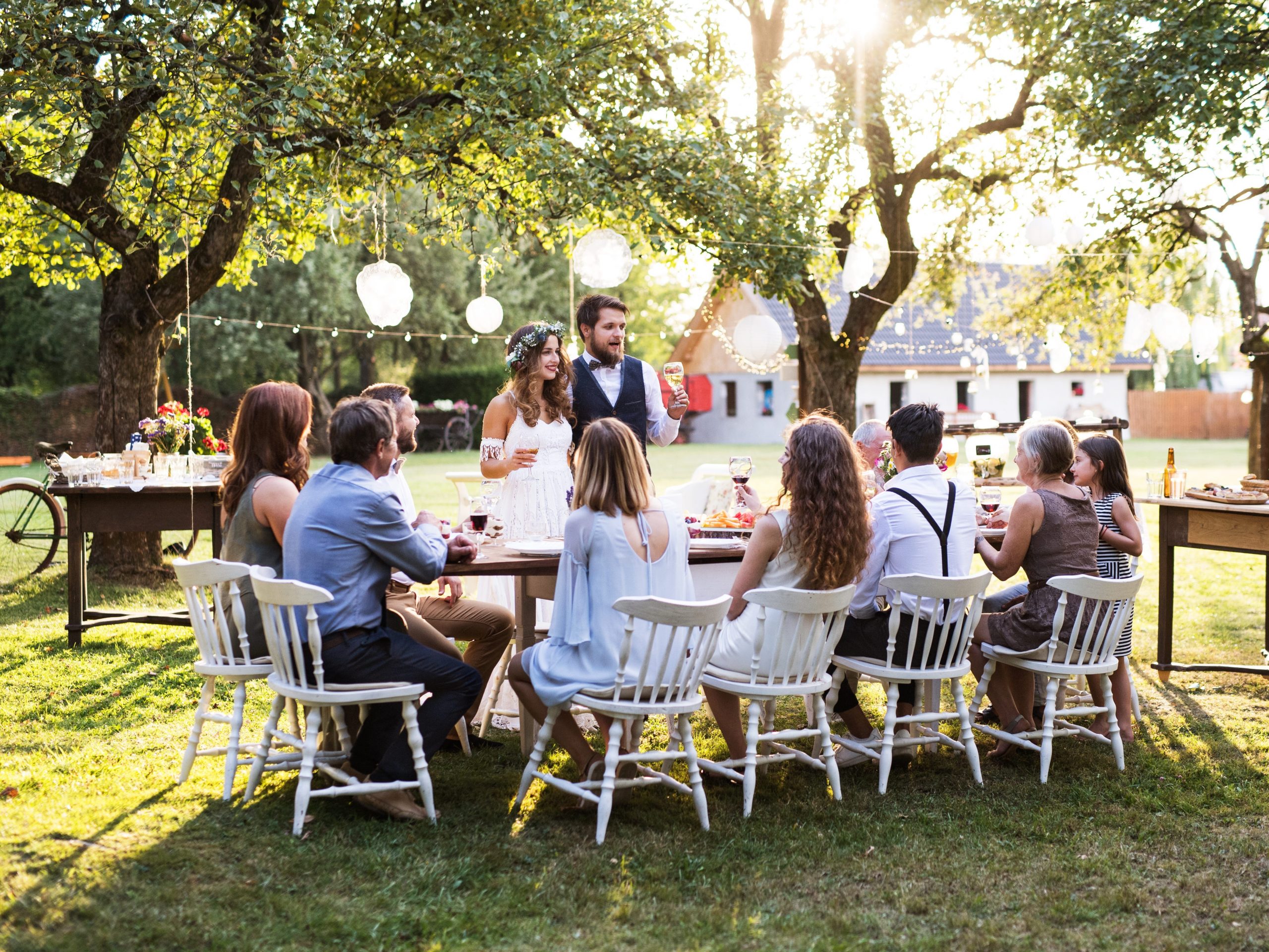 A couple gives a toast to a single table of guests in an outdoor setting during the day.