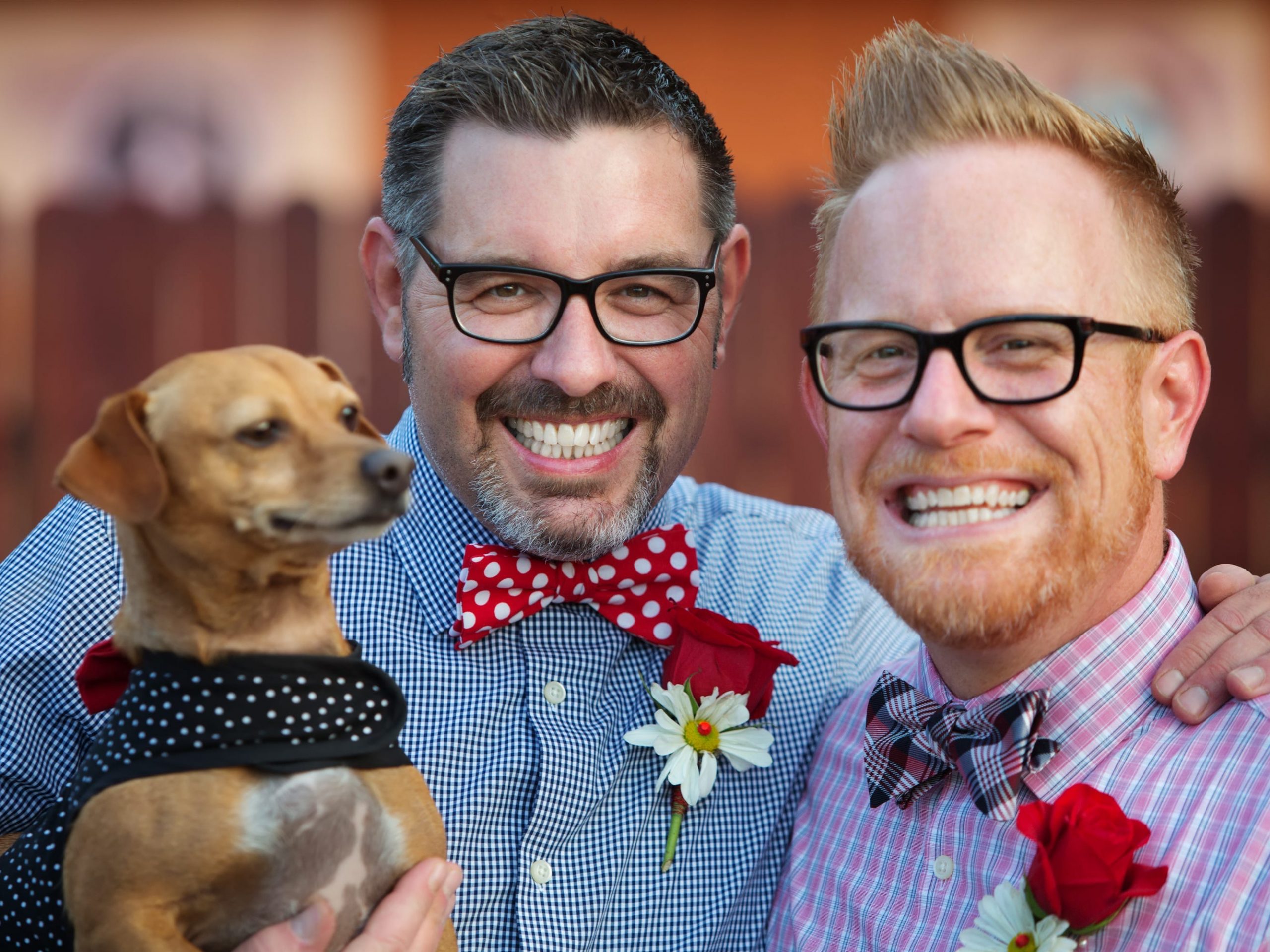 A male couple smile and hold their pet dog.