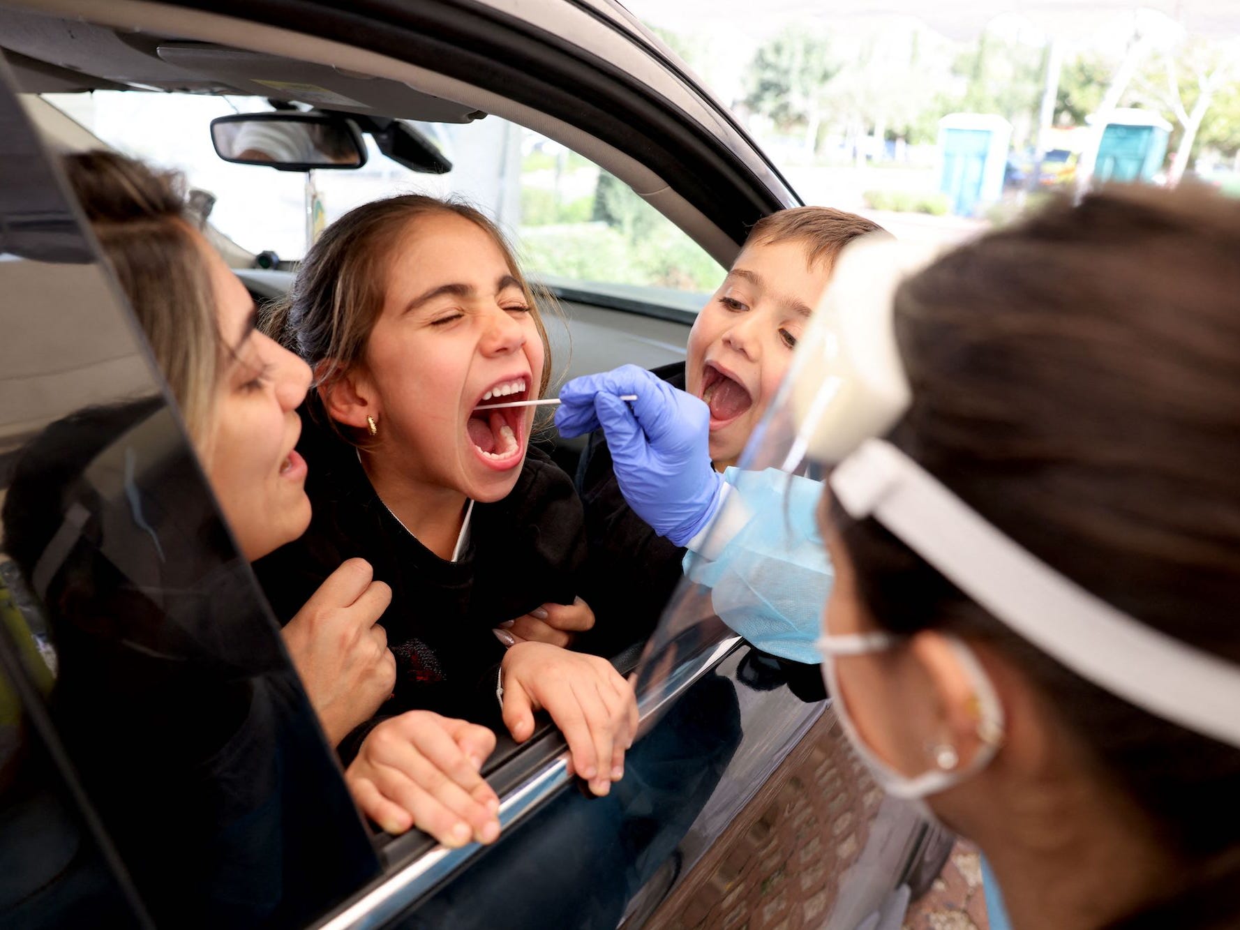 A child is getting tested for COVID-19 while leaning out of a car window.