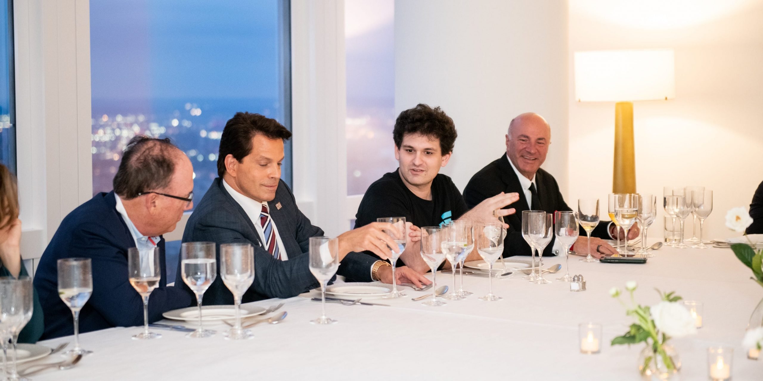 Sam Bankman-Fried is shown sitting at a long white table having dinner with Anthony Scaramucci  and Shark Tank investor Kevin O'Leary.