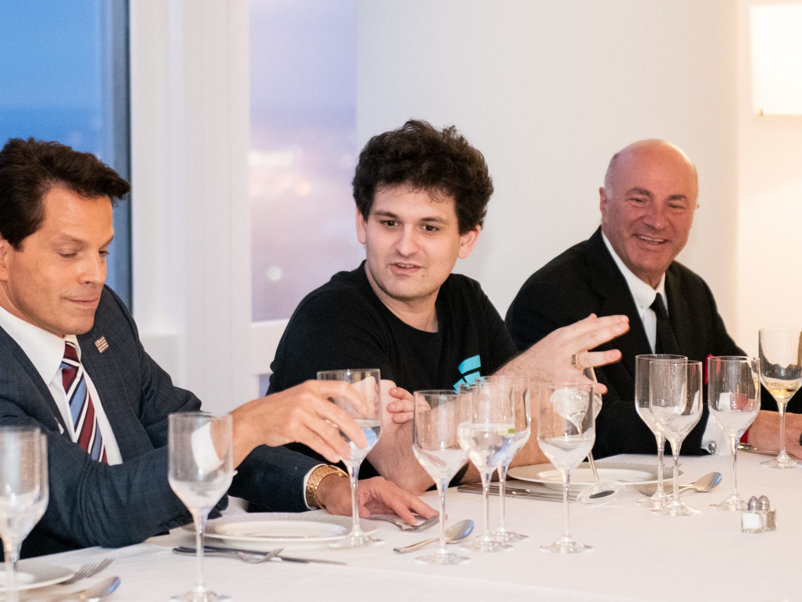 Sam Bankman-Fried is shown sitting at a long white table having dinner with Anthony Scaramucci  and Shark Tank investor Kevin O'Leary.