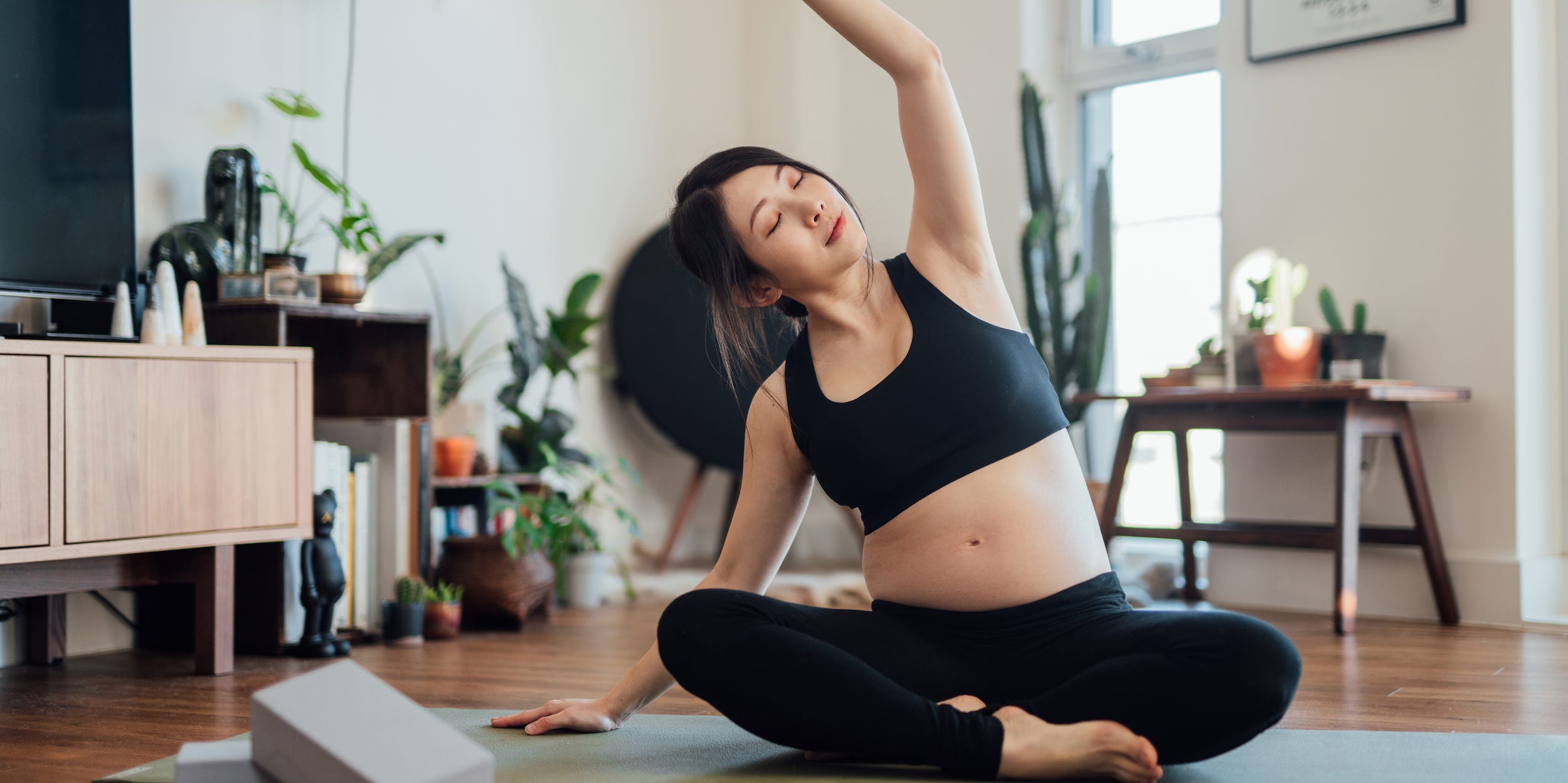 A pregnant woman does yoga on a mat at home.