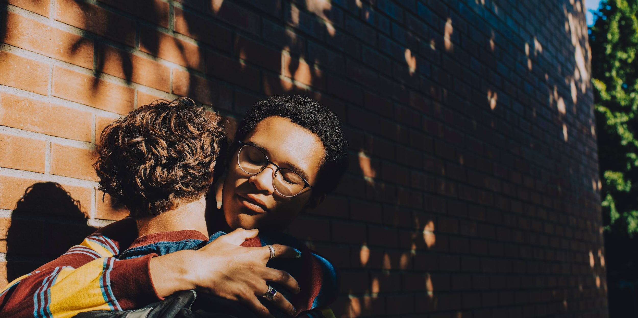 Two friends embrace in the shadow of a tree.