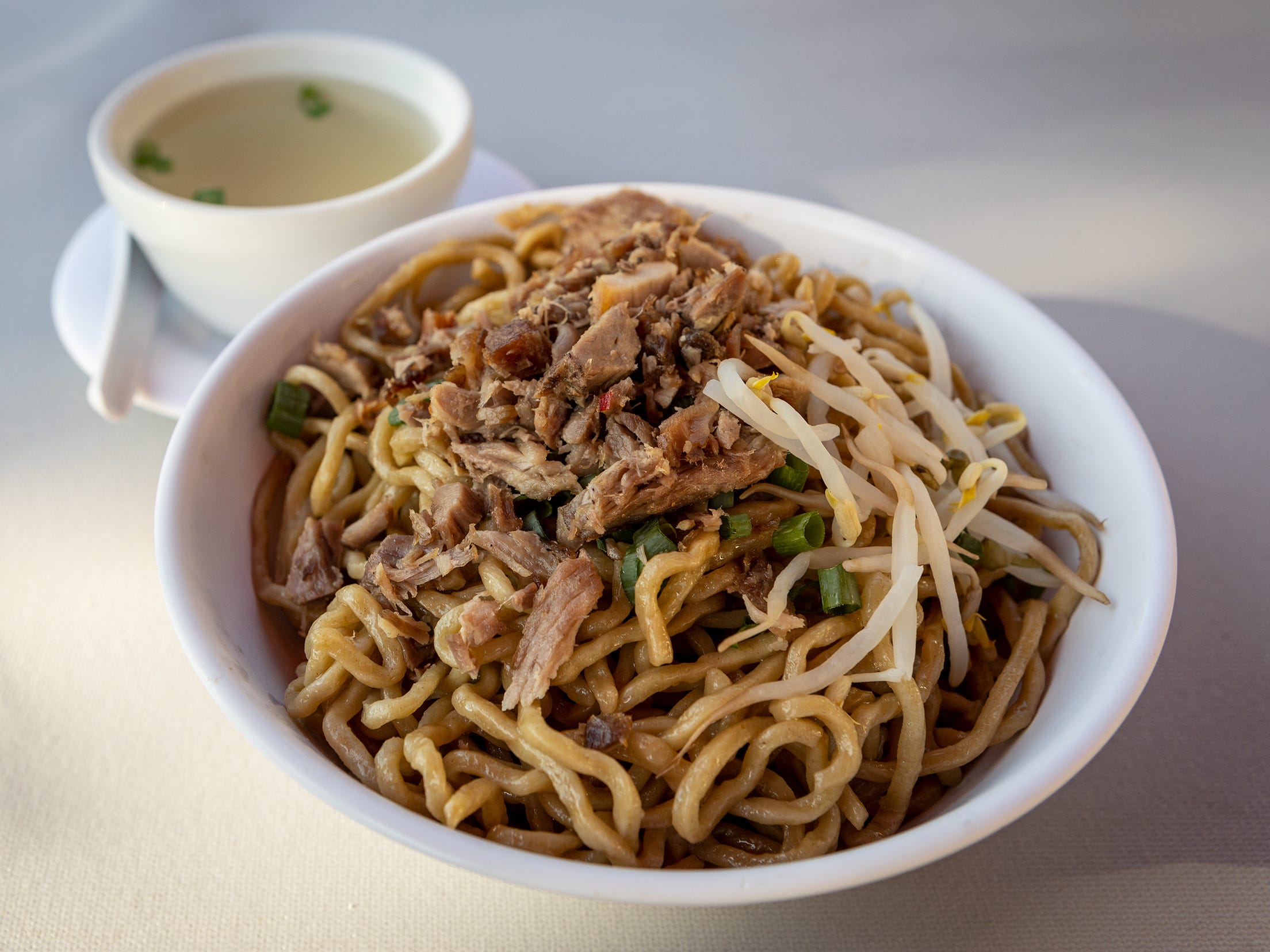 A noodle dish in a bowl with a smaller bowl of soup.