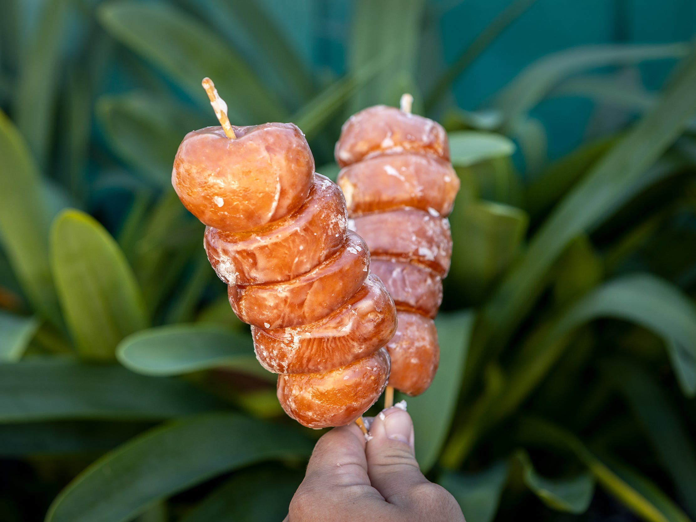 A hand holding a stack of small dessert pastries on skewers.