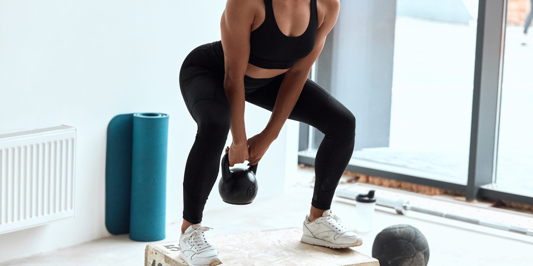 A woman in workout attire performs a kettle bell swing.