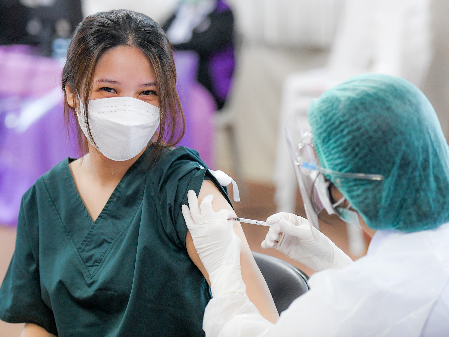 healthcare worker in mask, smiling, getting booster shot.