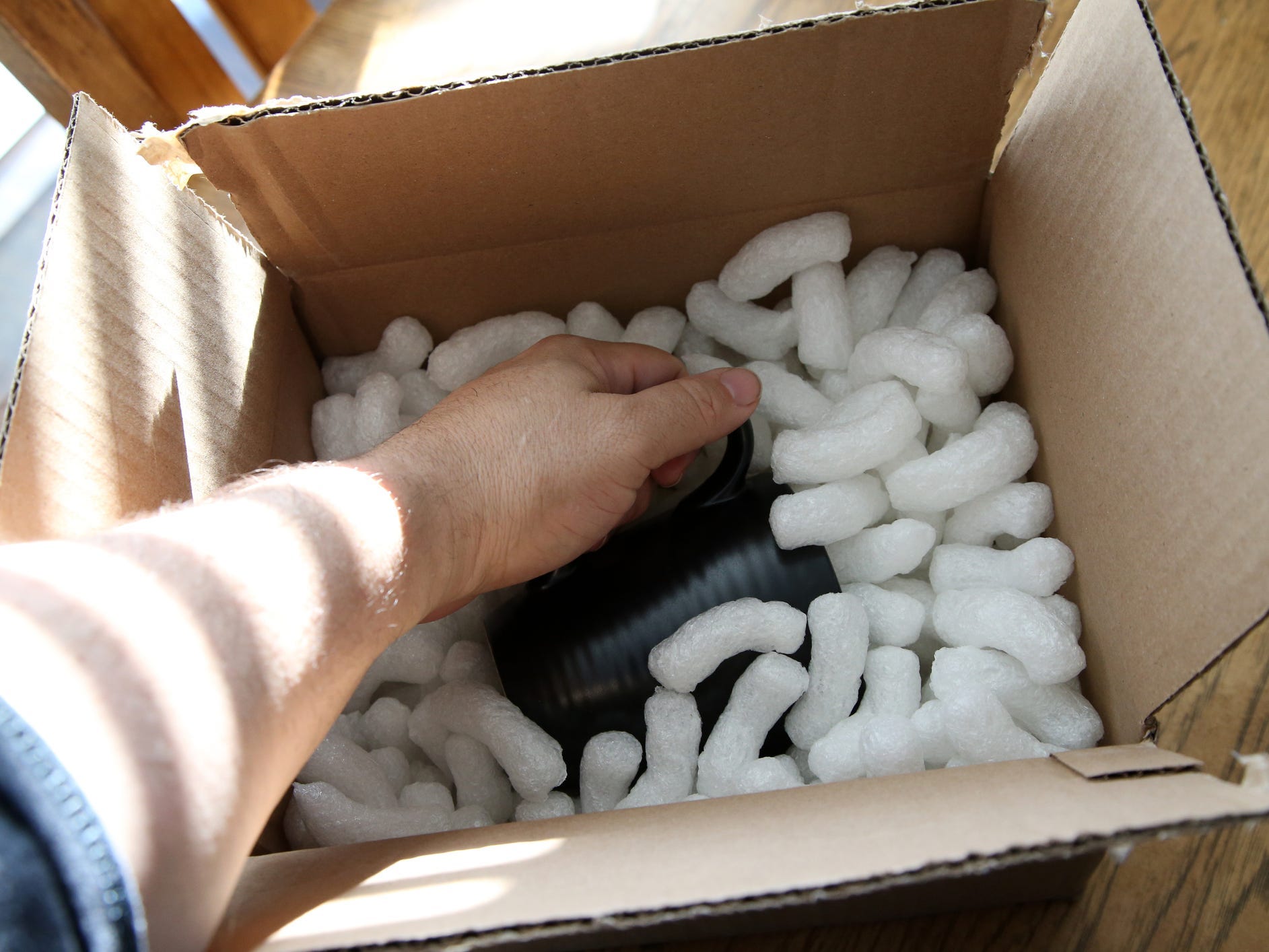 Person grabbing for a mug in a box with packing peanuts