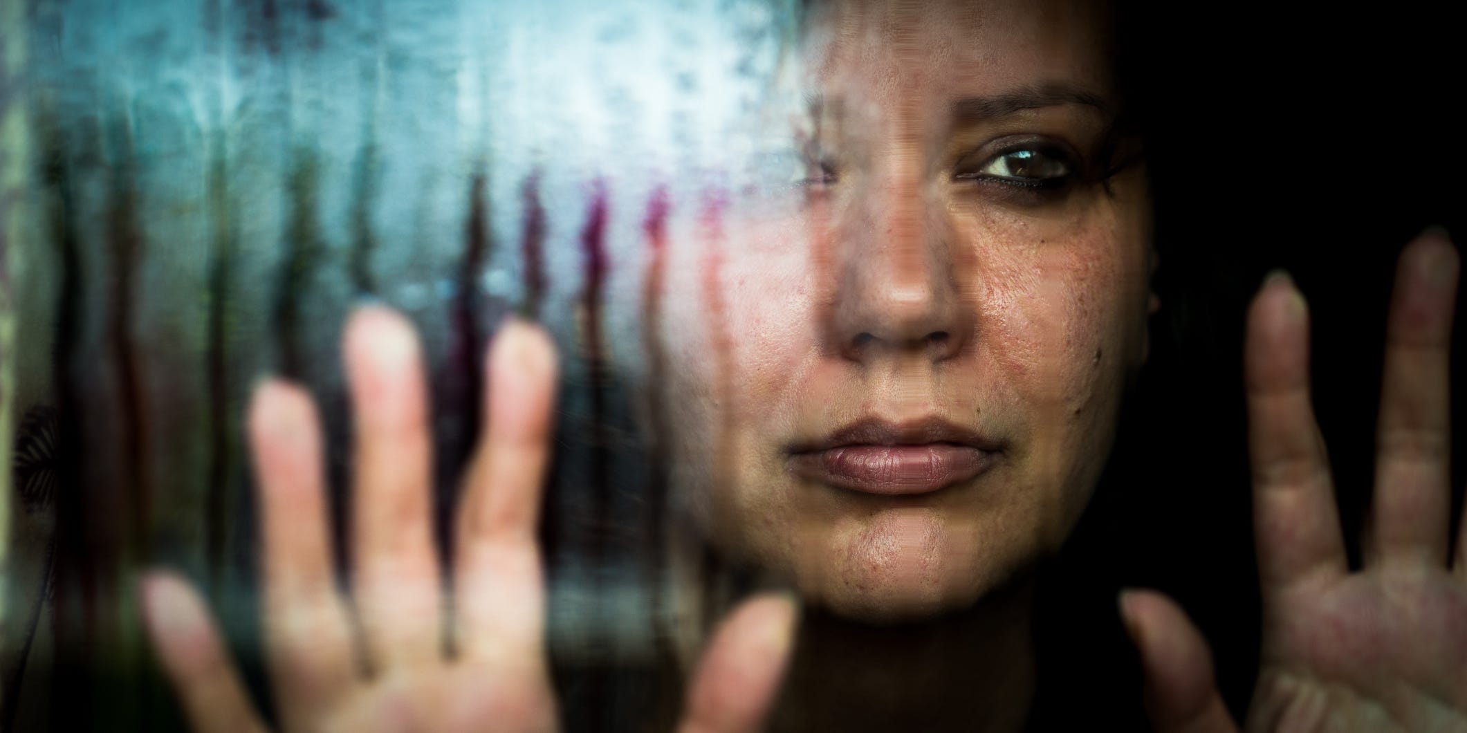 A woman stands behind a glass window avoiding the rain outside.