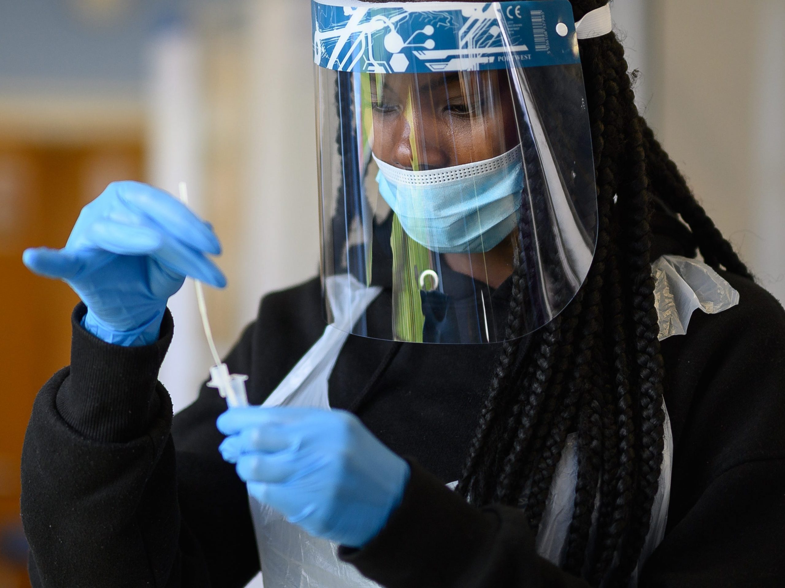 Woman wearing person protective equipment processes a swab test.