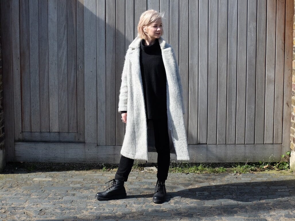 photo of woman in white coat standing in front of gate