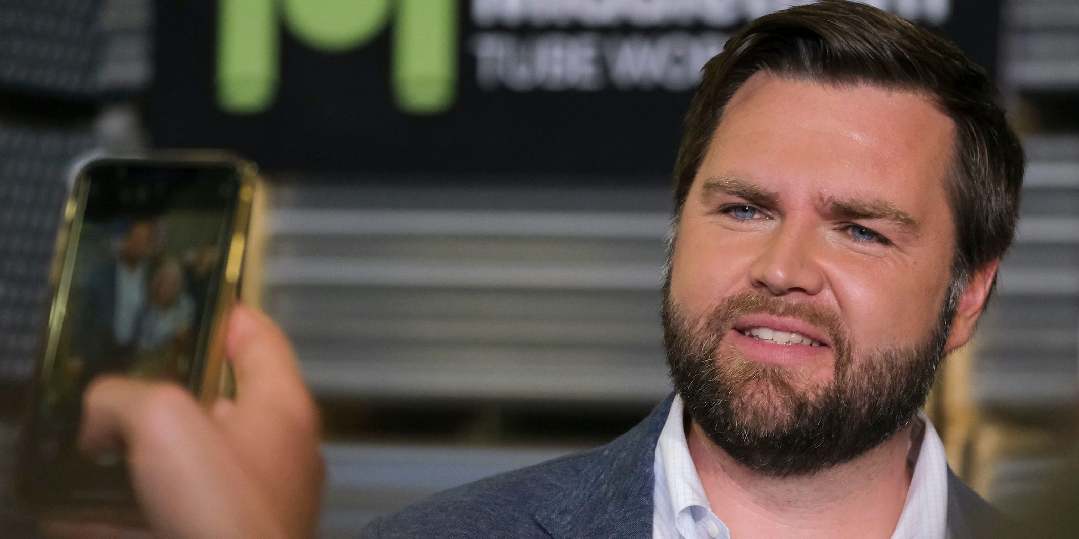 J.D. Vance stands in front of a smartphone taking a picture of him.