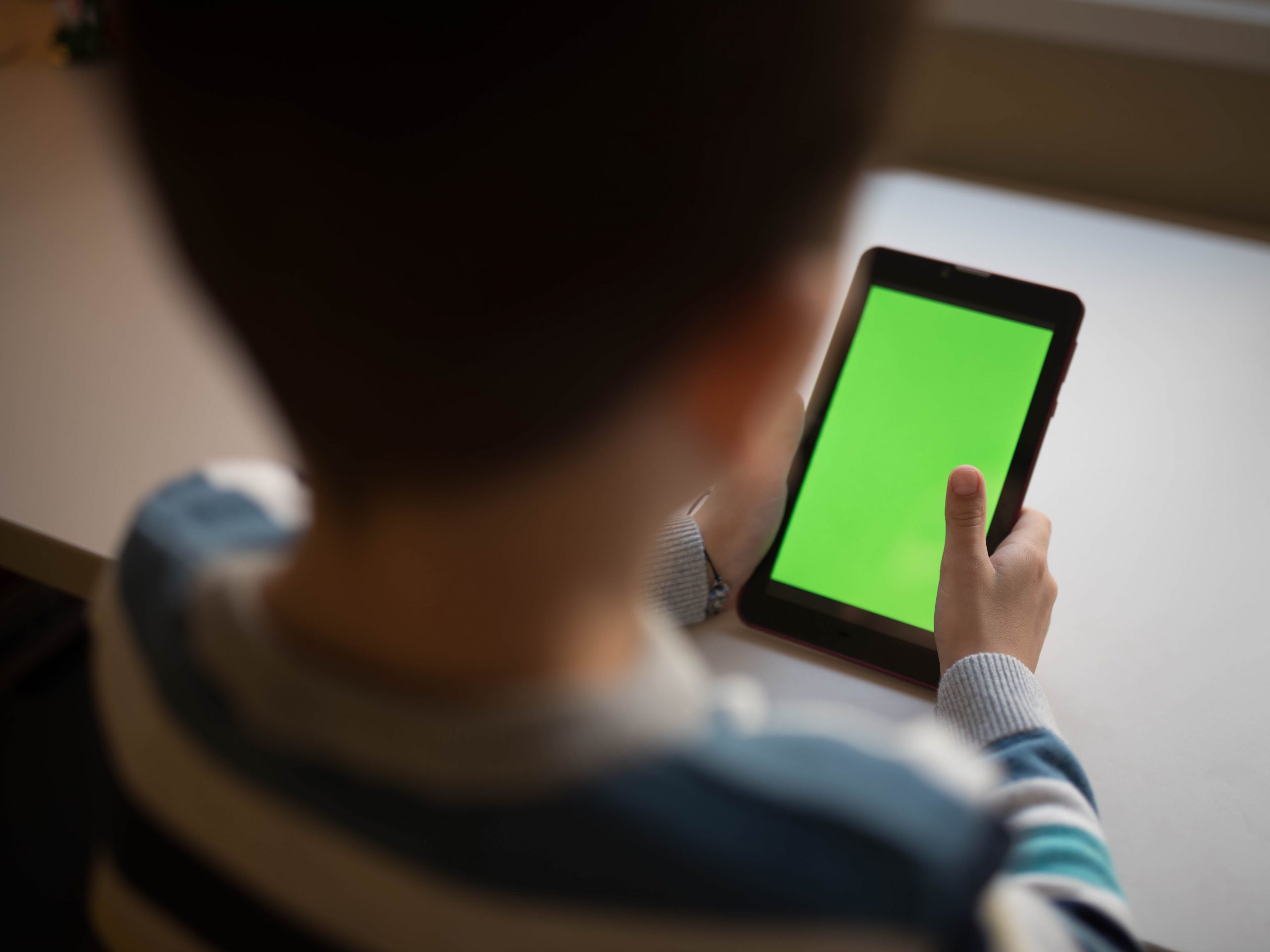 a little boy sitting at a desk with a green screen tablet - stock photo
