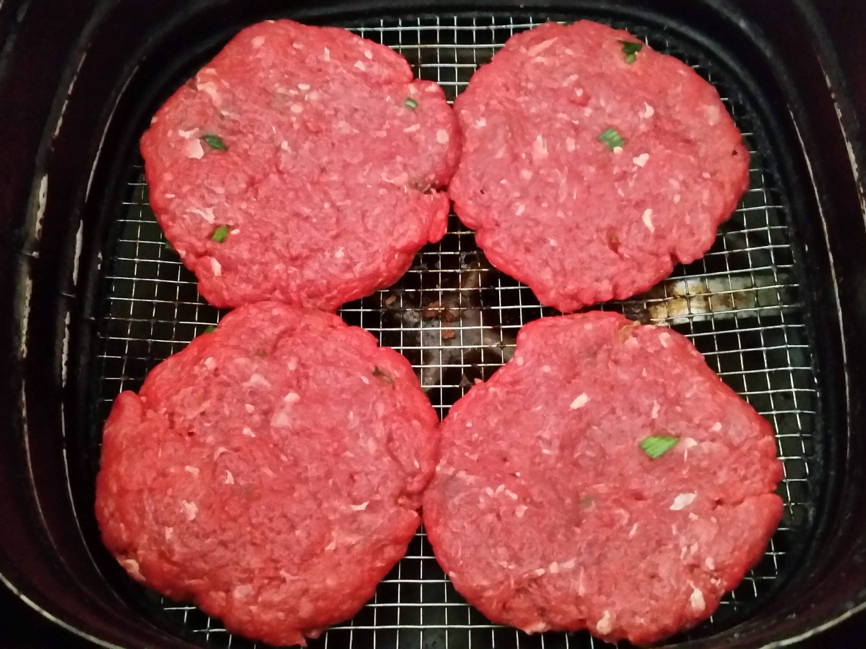 Four raw hamburger patties in the basket of an air fryer