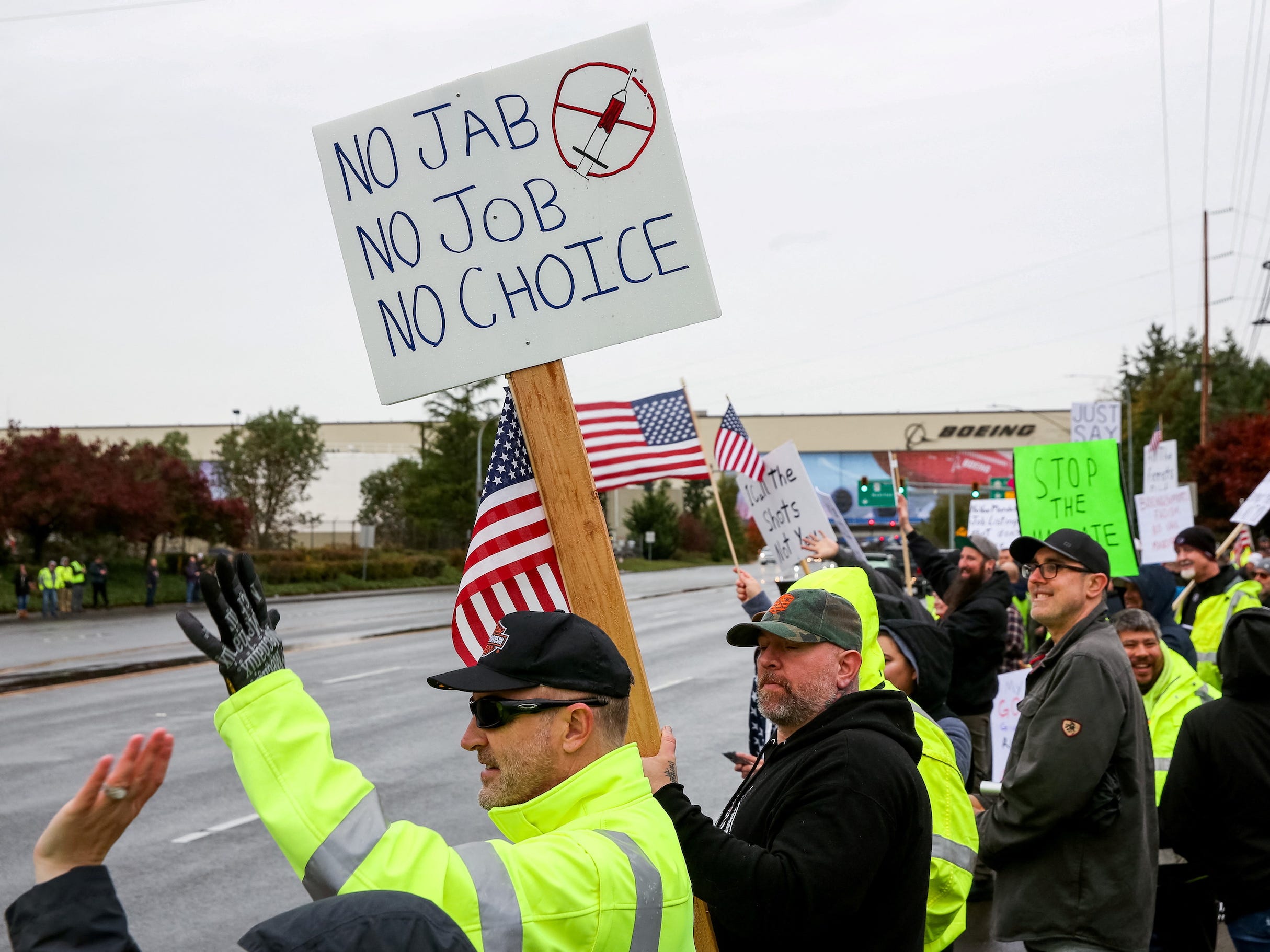 men holding american flags protest on roadside with sign reading "no jab no job no choice"